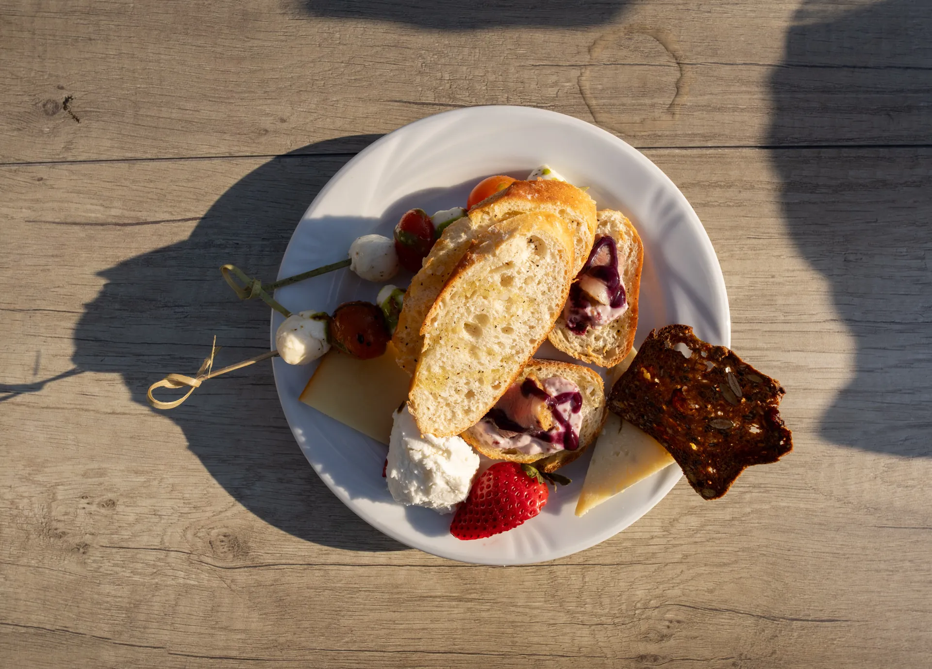 A plate of appetisers, bread, cheese and berries, on the deck