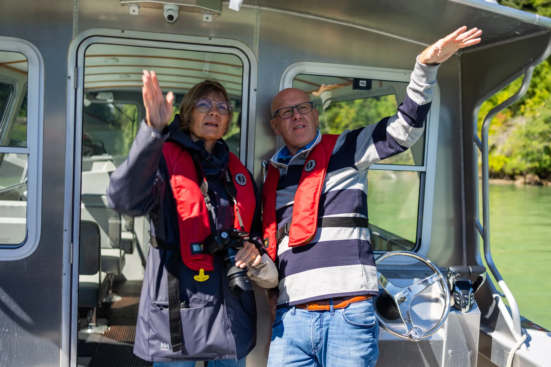 A couple in red life jackets waving from the open boat on the way out