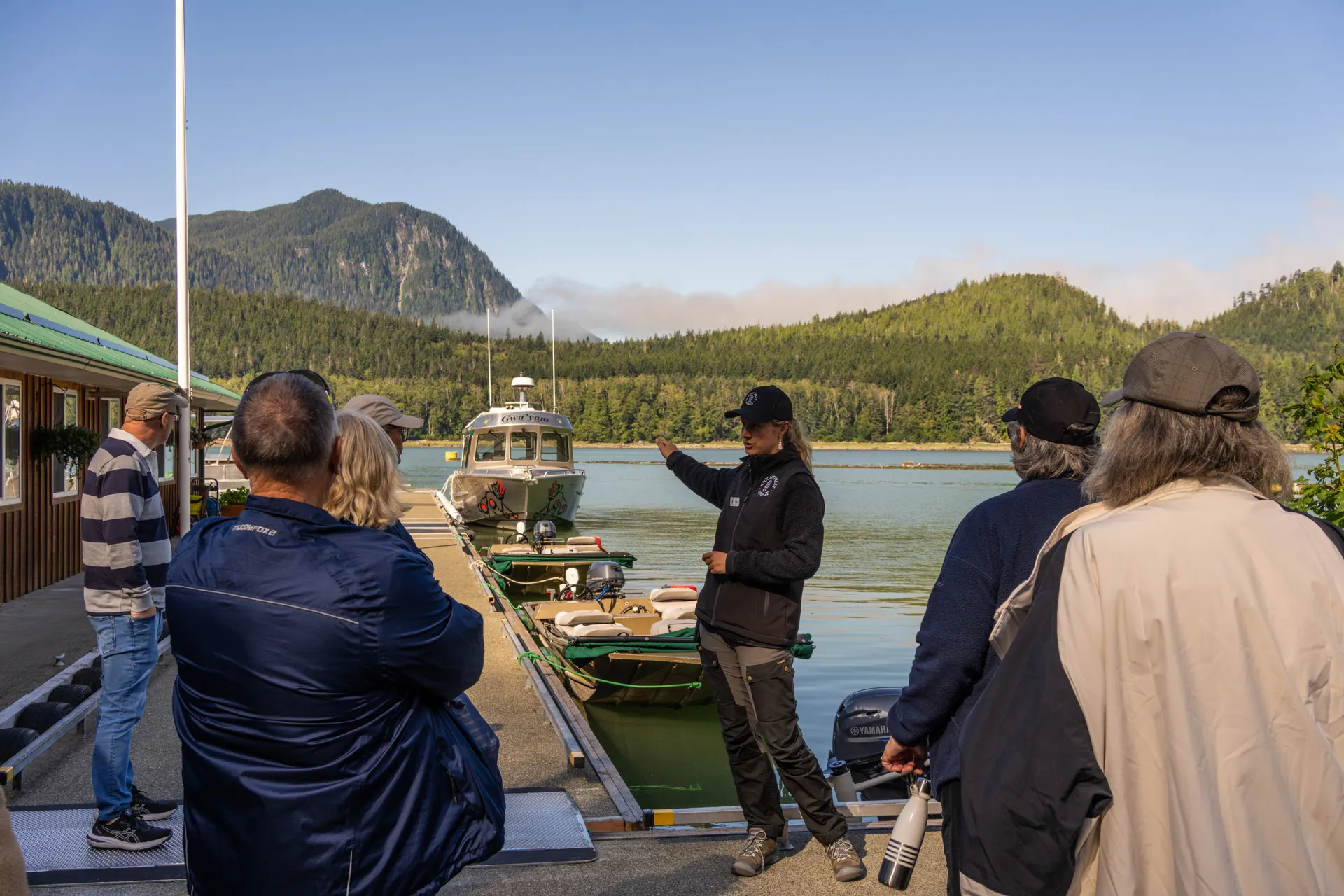 A guide on the lodge dock briefing a group of guests before the boats go out, pointing across the cove