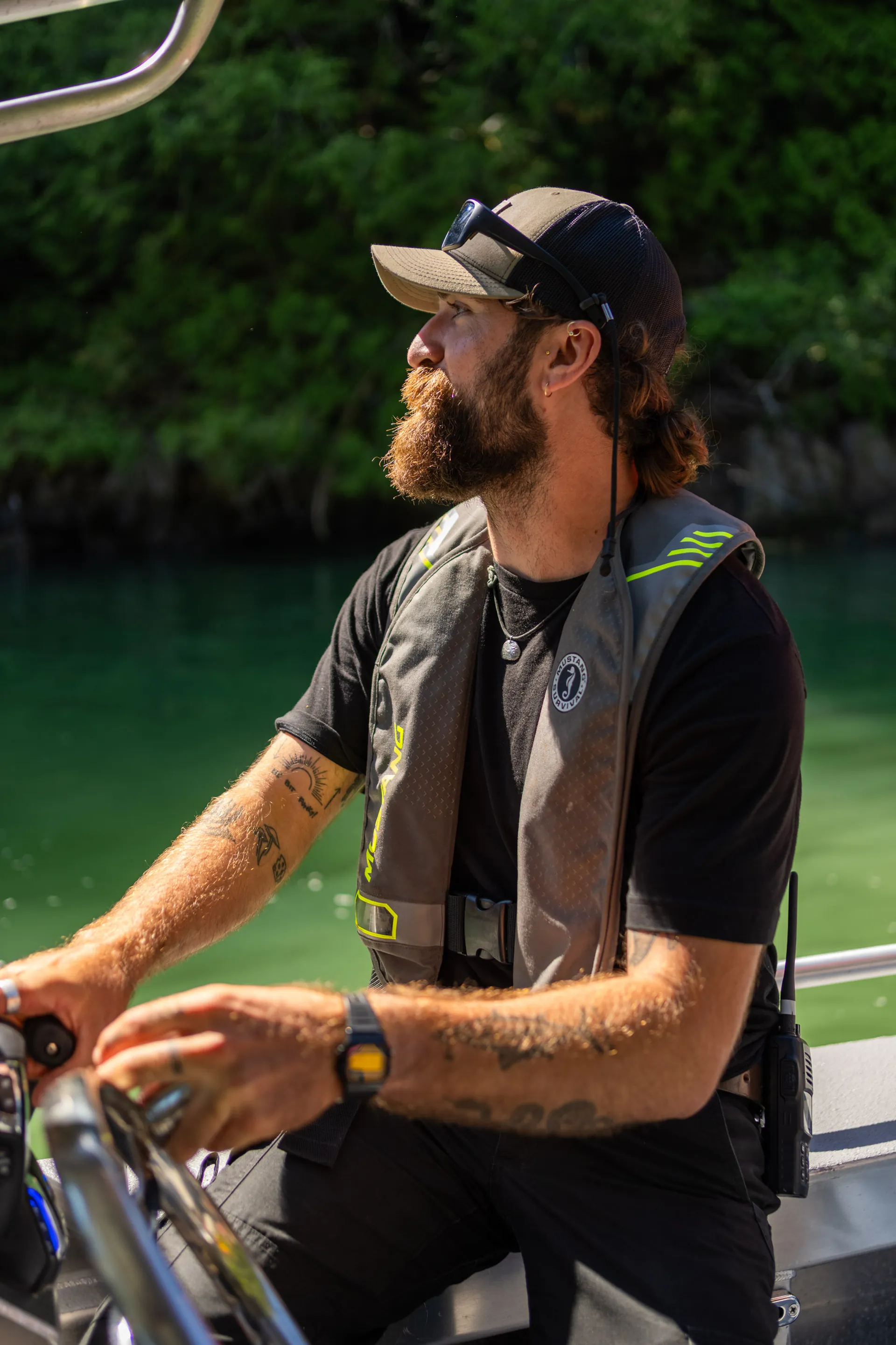 A guide at the helm of the boat, cap and beard, watching the shore
