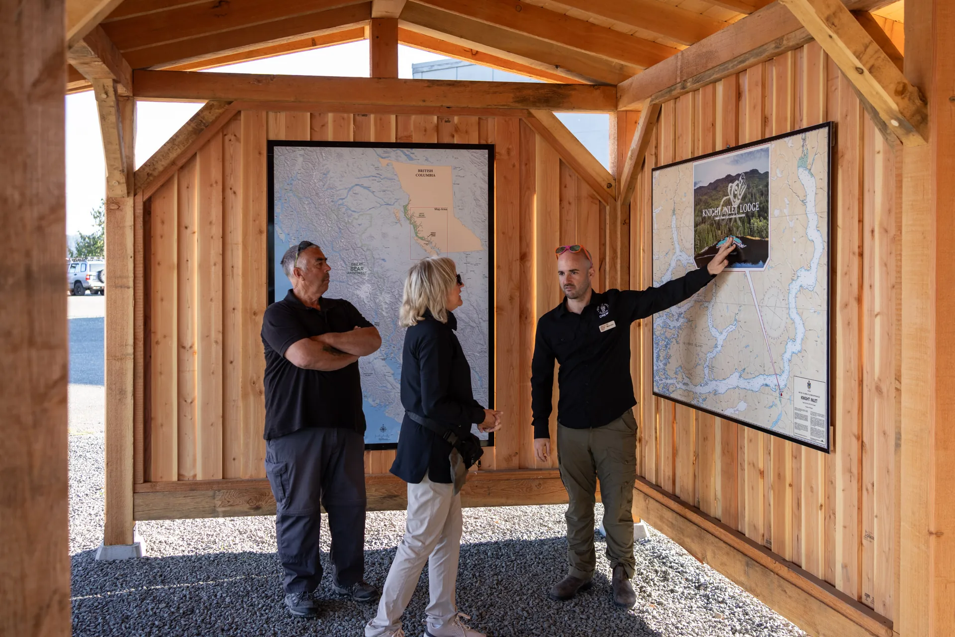 Two guests with a guide at the map board in the timber shelter, the inlet's channels laid out