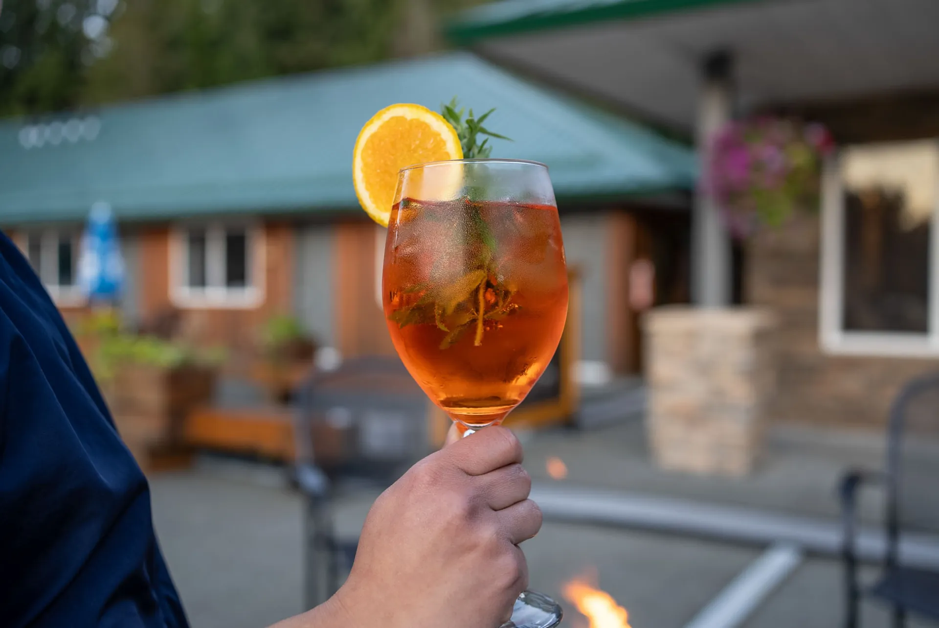 An Aperol spritz held up on the lodge deck in the evening, the green roof behind