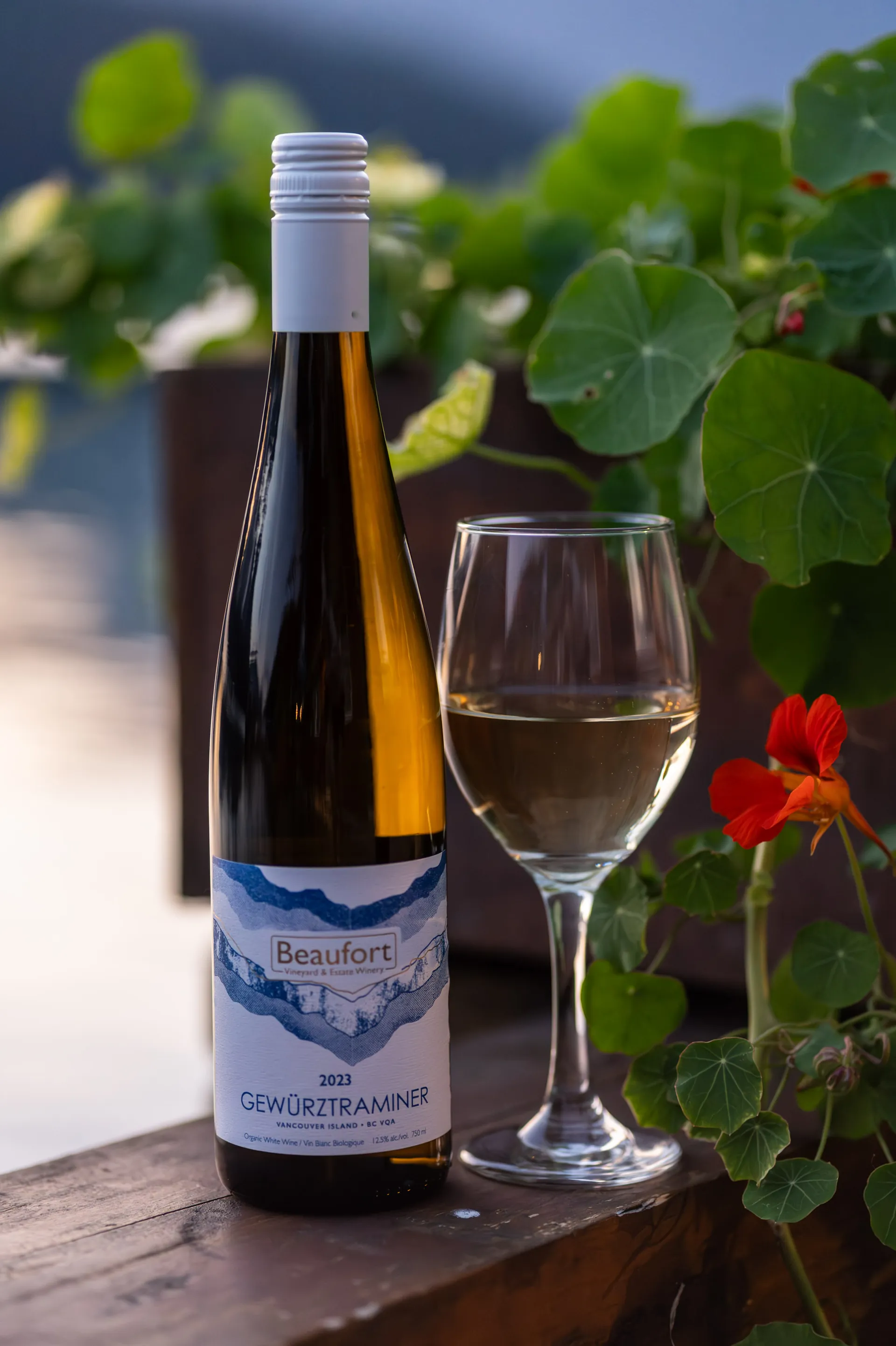 A bottle and a glass of white wine on the deck rail among the flowers