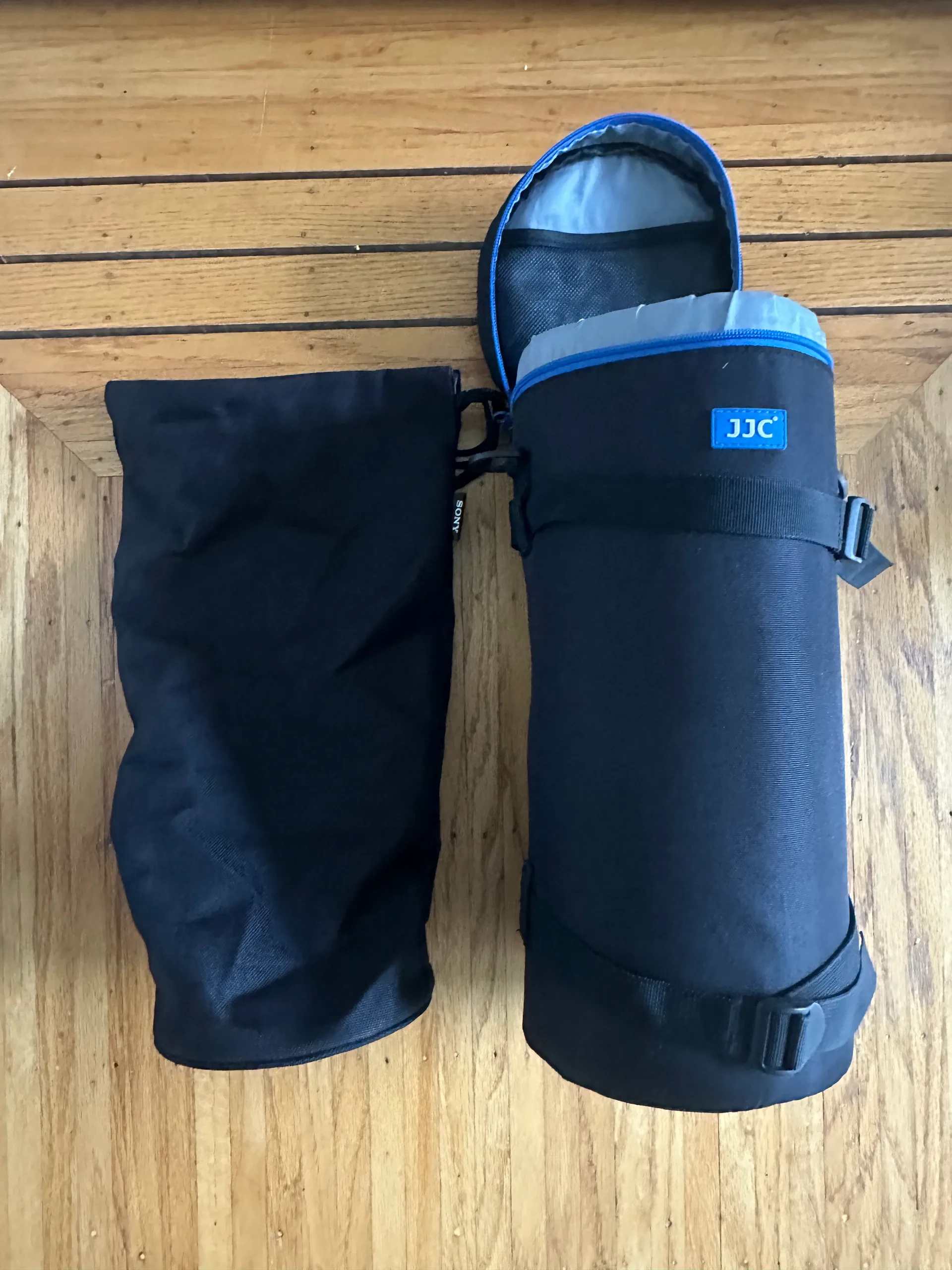 The padded JJC lens pouch for the 200-600 standing open on a wooden floor beside the black Sony lens hood bag