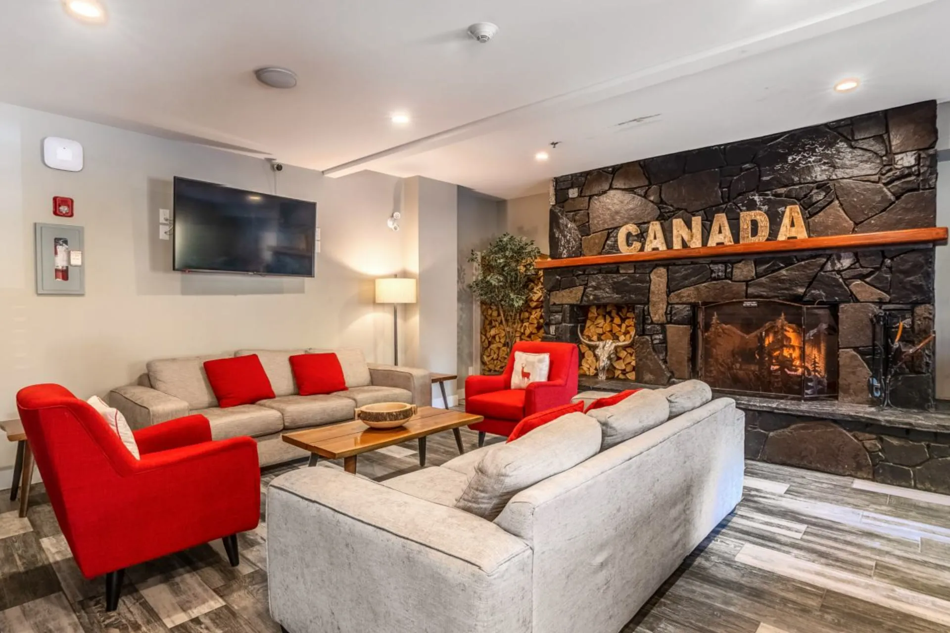 The great room at Basecamp Lodge Canmore, red armchairs and a sofa in front of the stone fireplace with its CANADA sign