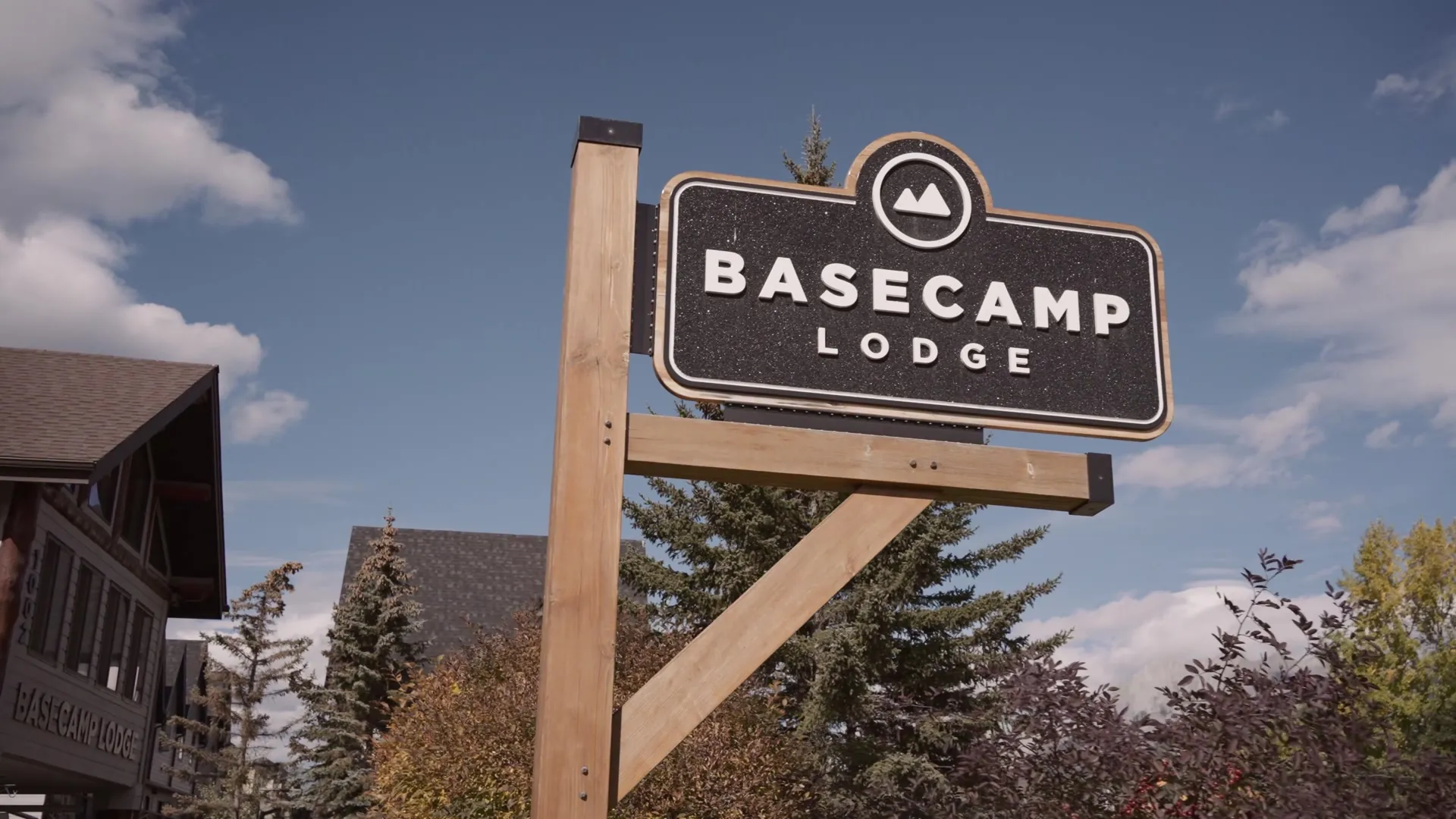 The Basecamp Lodge sign on a timber post against a blue sky