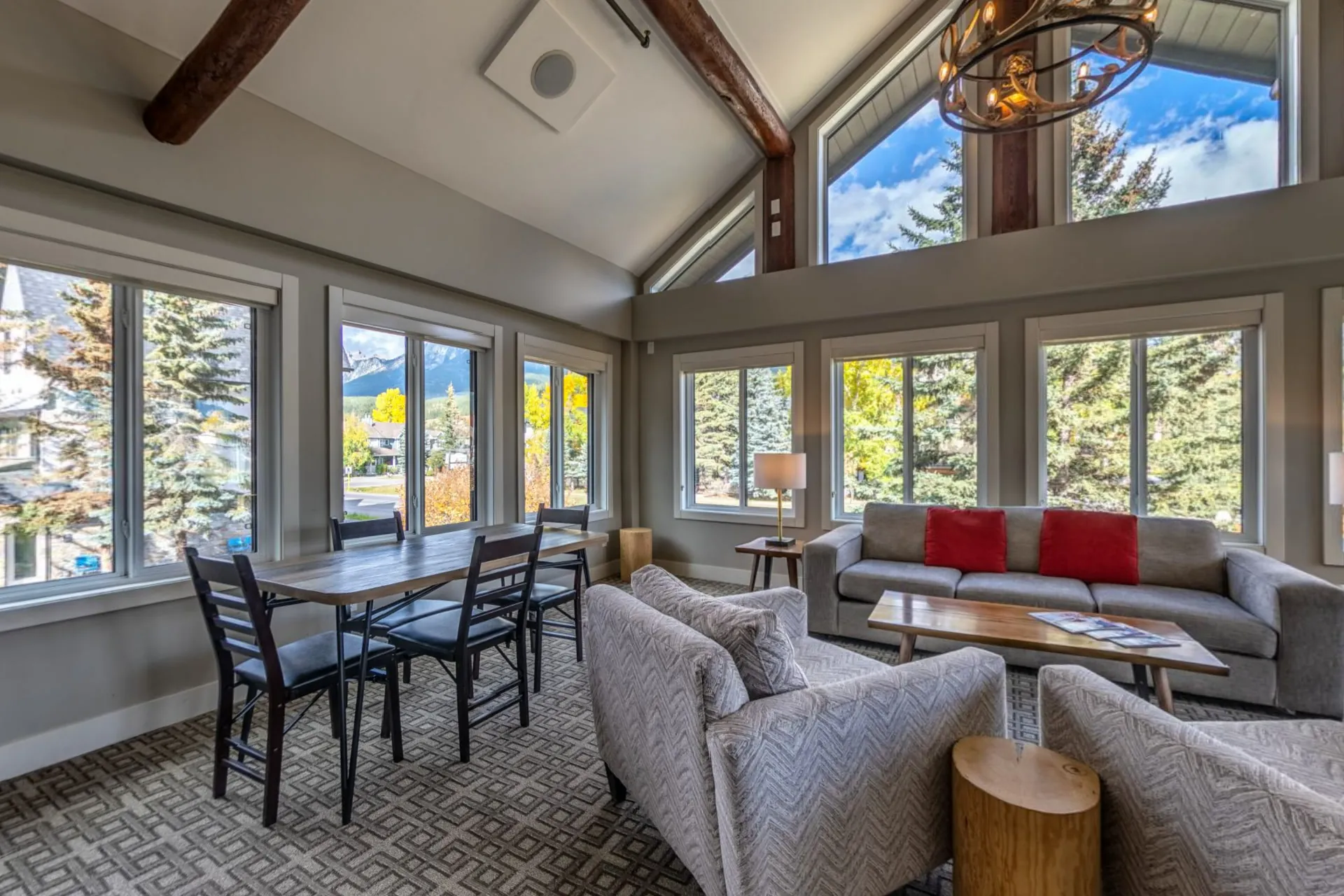 The great room's dining table and armchairs under tall windows with the mountains outside