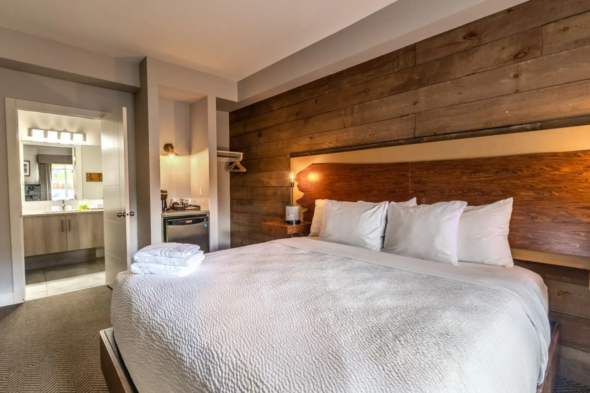 A deluxe king room with a timber feature wall, white linen and the bathroom through the door