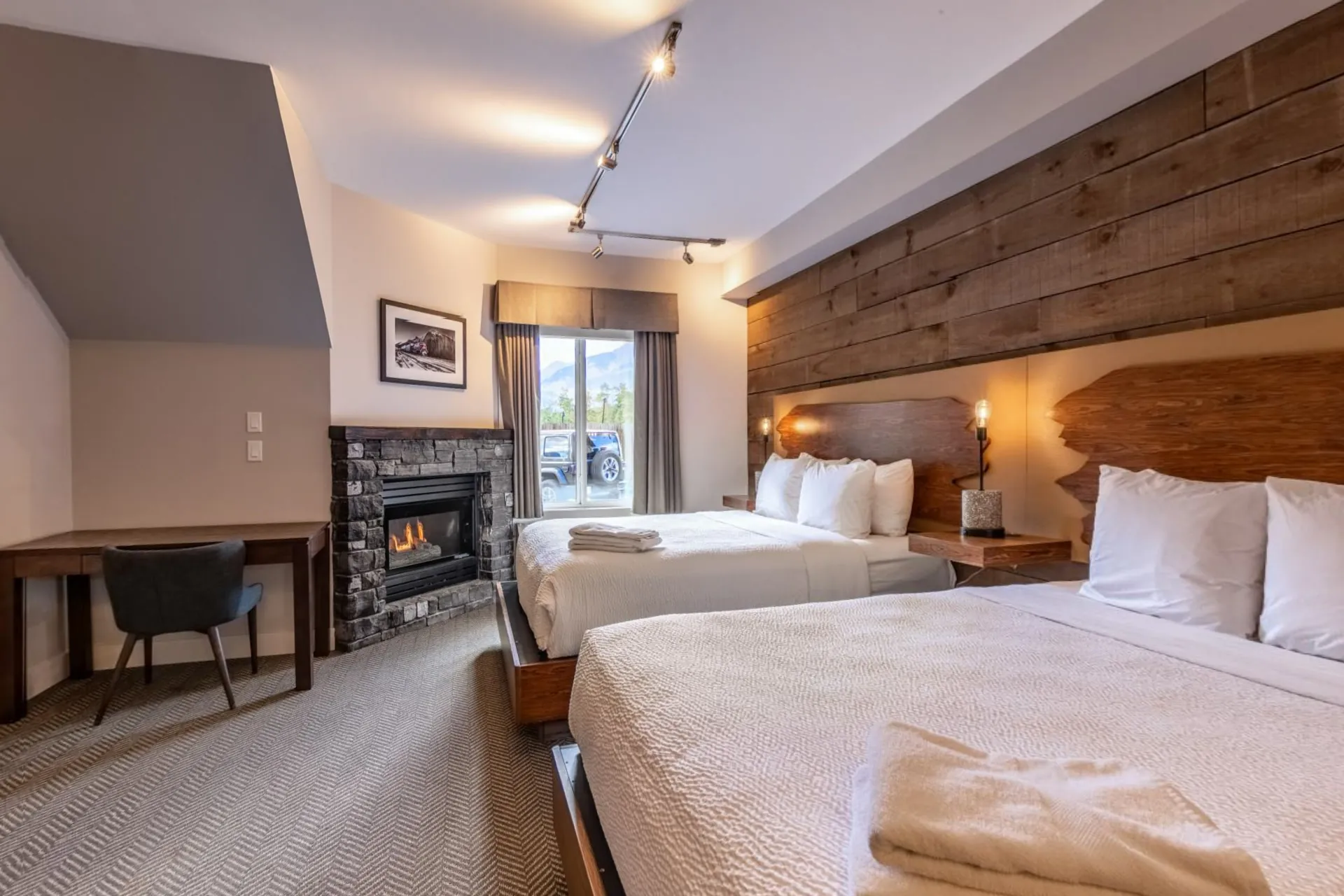 A deluxe double queen room with two beds, a desk and a gas fireplace