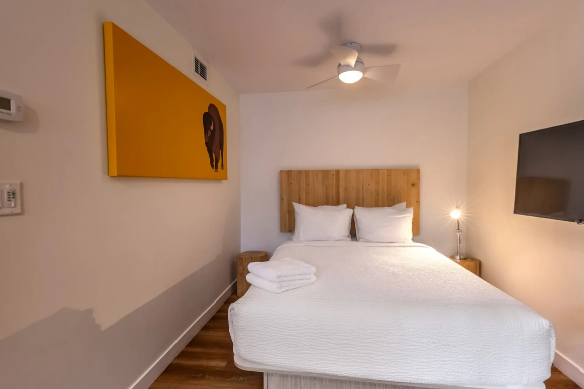 A micro studio with a queen bed, timber headboard and a bright yellow bear print