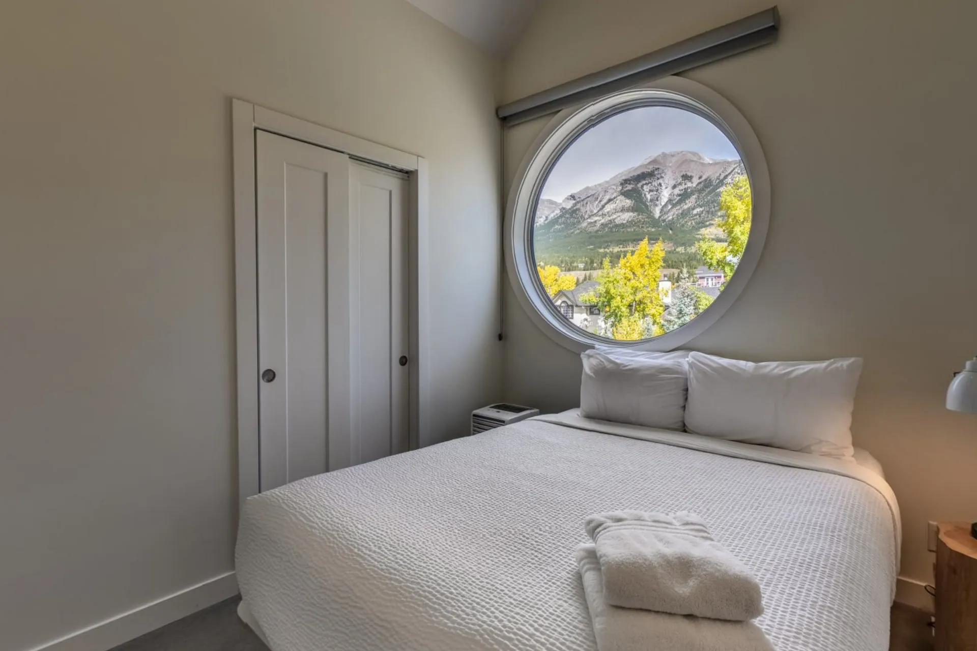 A bedroom with the round window framing the mountains, white linen and a sliding barn door