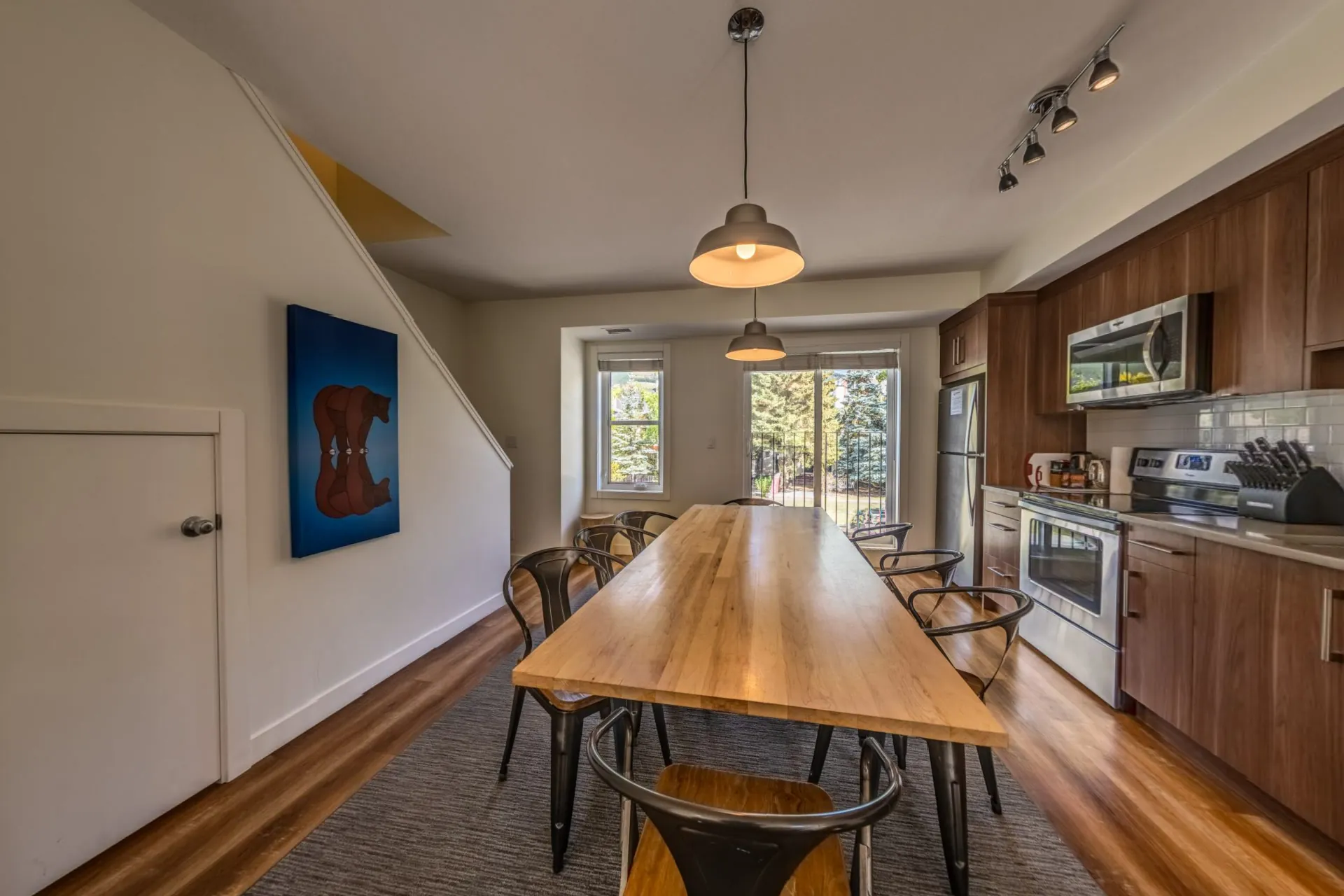 A three-bedroom suite's kitchen and dining area, a long timber table under pendant lights and mountain artwork
