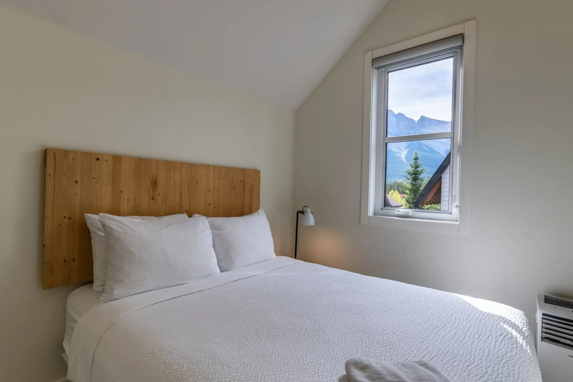 A high-ceilinged bedroom with a timber headboard and a window onto the peaks