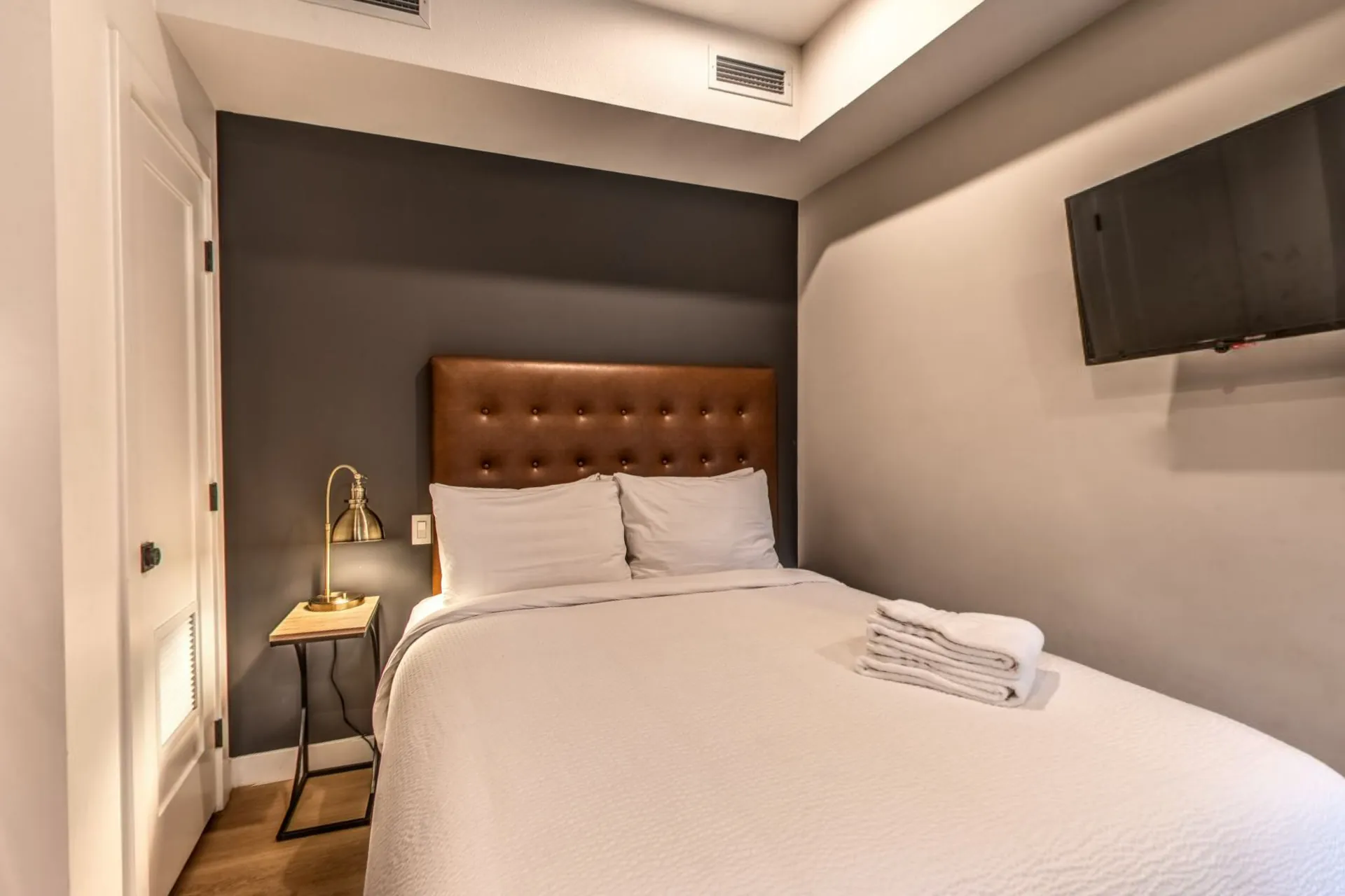 A micro studio, a queen bed with a leather headboard, a wall-mounted television and a door to the patio