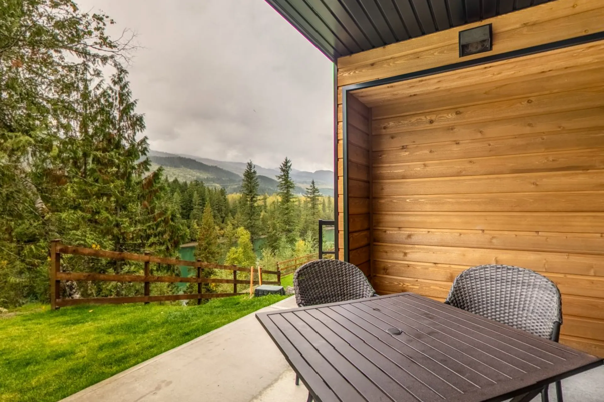 A micro studio's private patio with a table and chairs, cedar cladding and the river valley through the trees