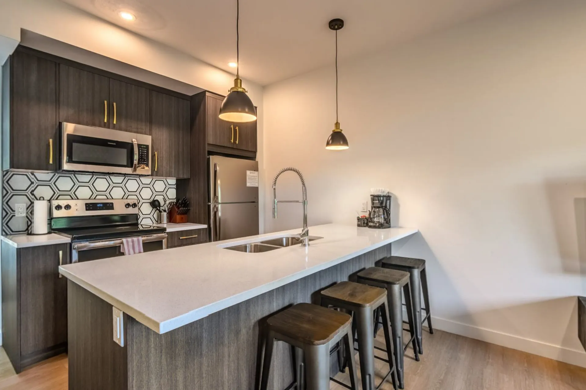 A one-bedroom suite's kitchen with a breakfast bar, stools, pendant lights and a full set of appliances