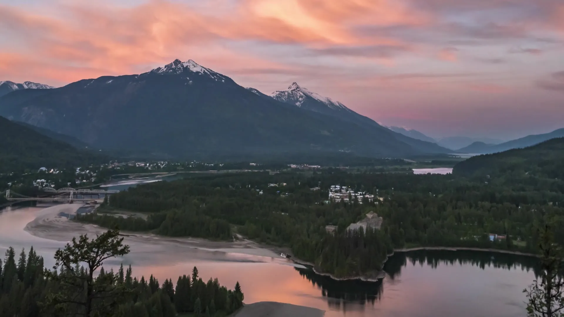 Sunset over a mountain lake outside Revelstoke, pink cloud above the peaks and the town lights below