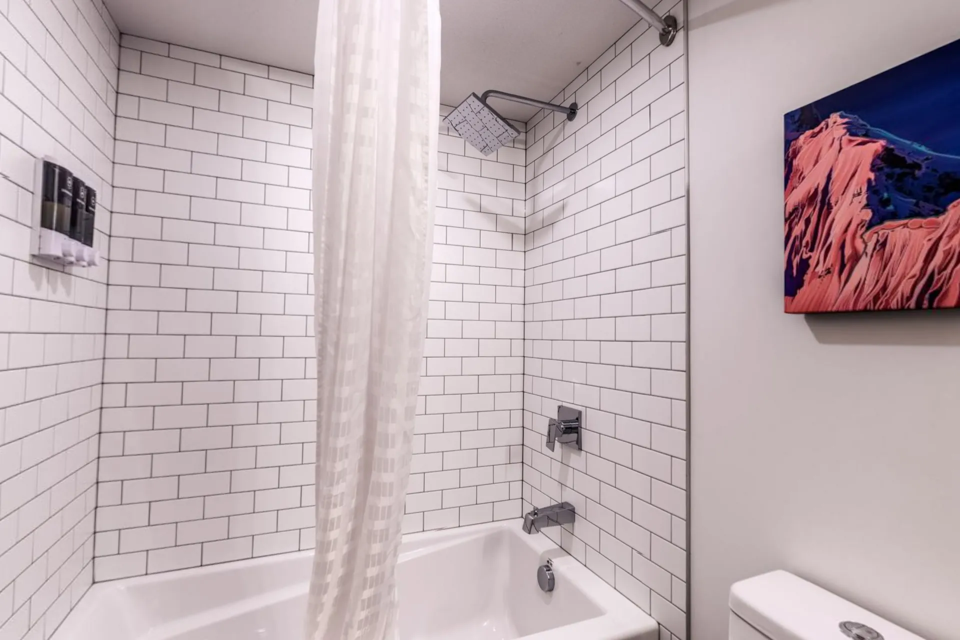A bathroom with white subway tile, a tub and shower and a mountain print on the wall