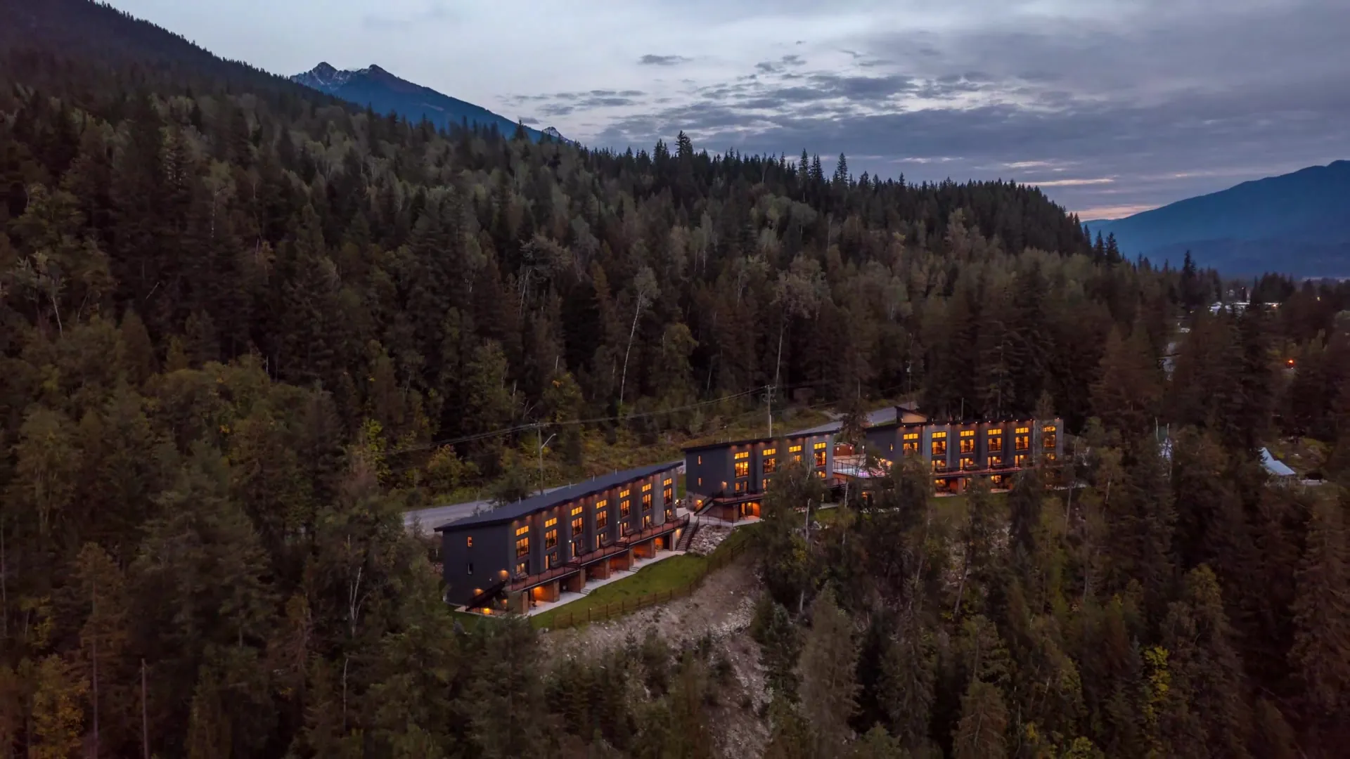 The Revelstoke suites lit at dusk on the bluff, every window glowing against the dark forest and the mountains behind