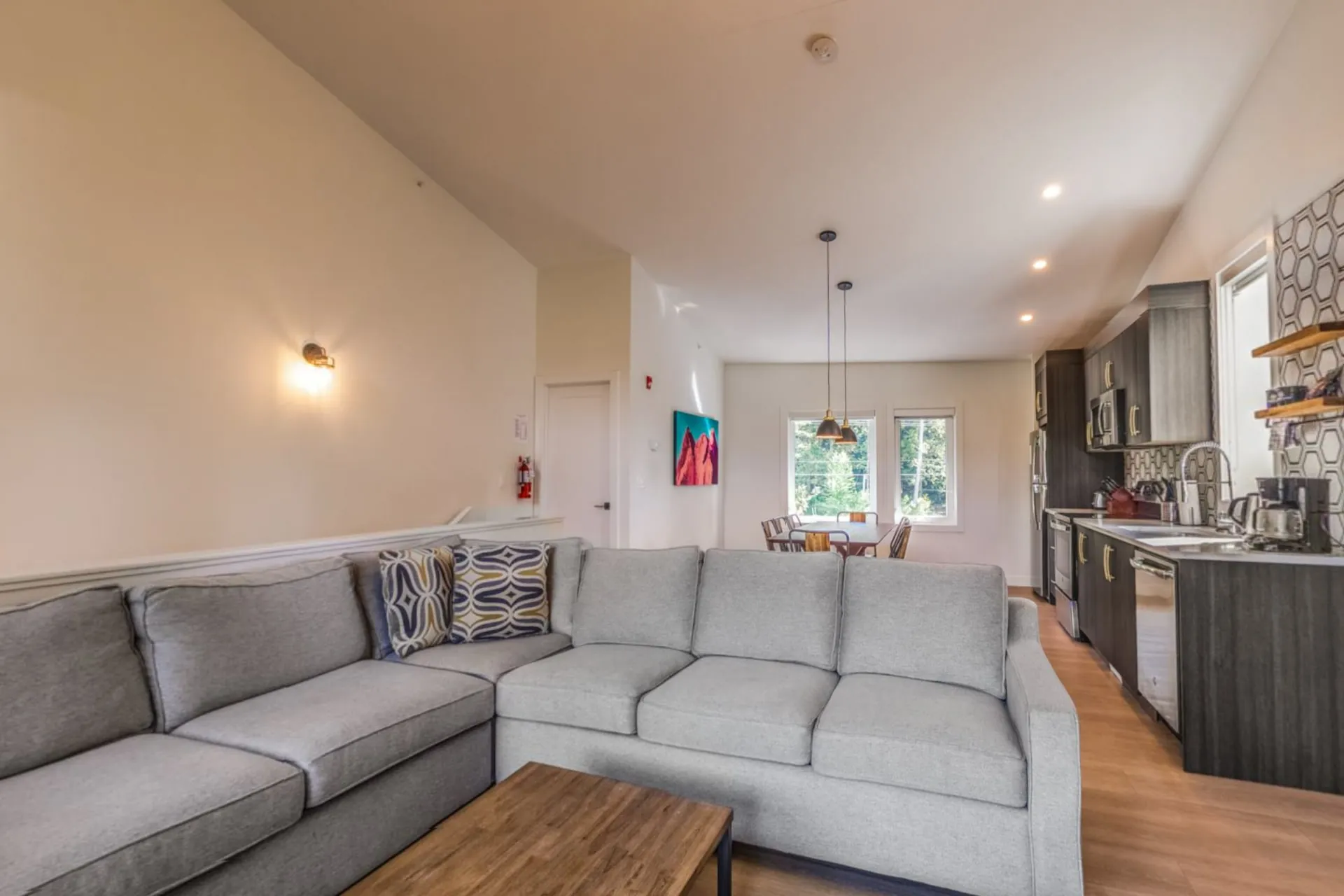 A three-bedroom suite's living area, a large grey sectional facing the open kitchen and dining table under vaulted ceilings