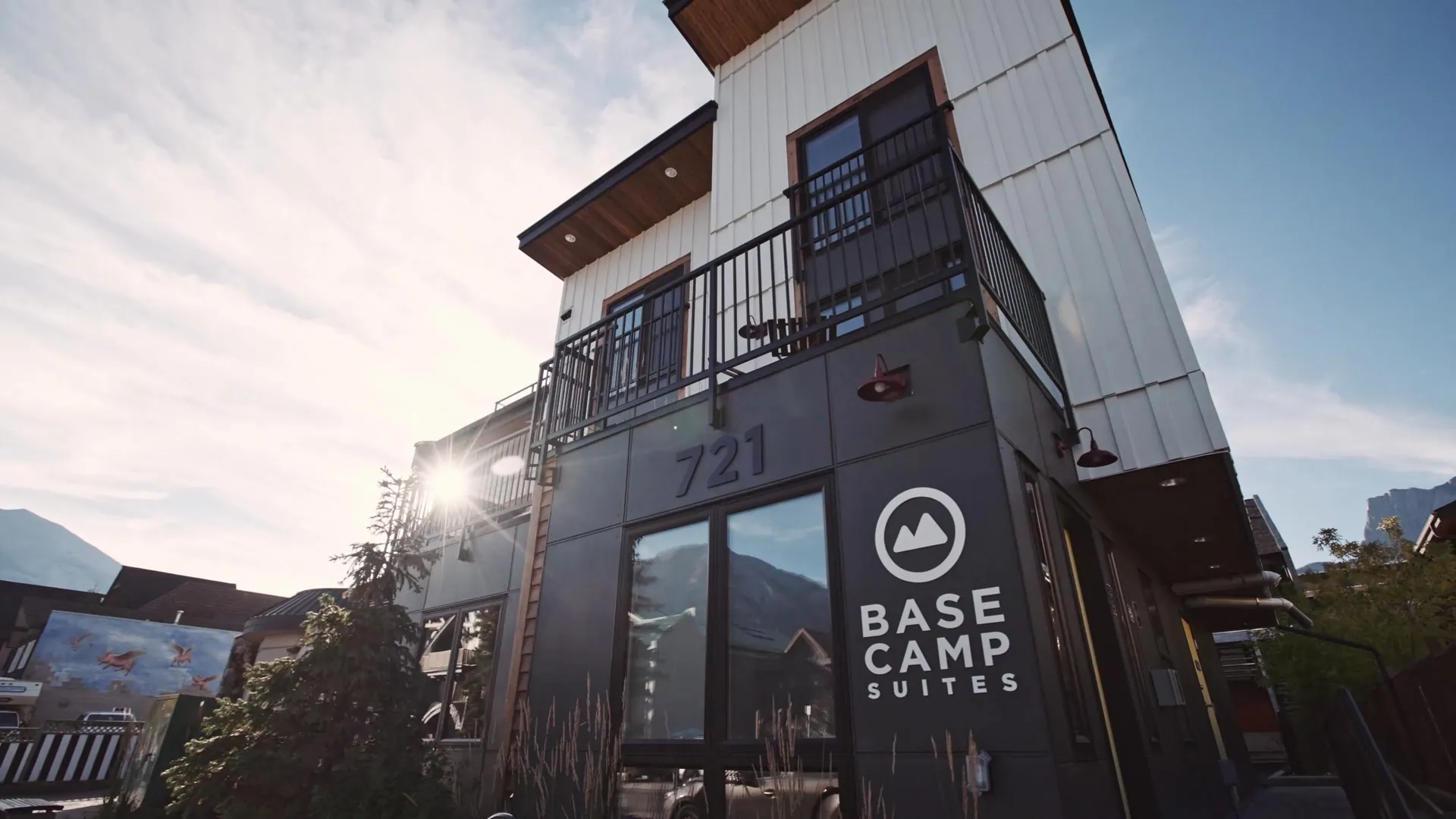 The entrance of Basecamp Suites Canmore at 721 10th Street, the sign on dark cladding with the sun flaring behind