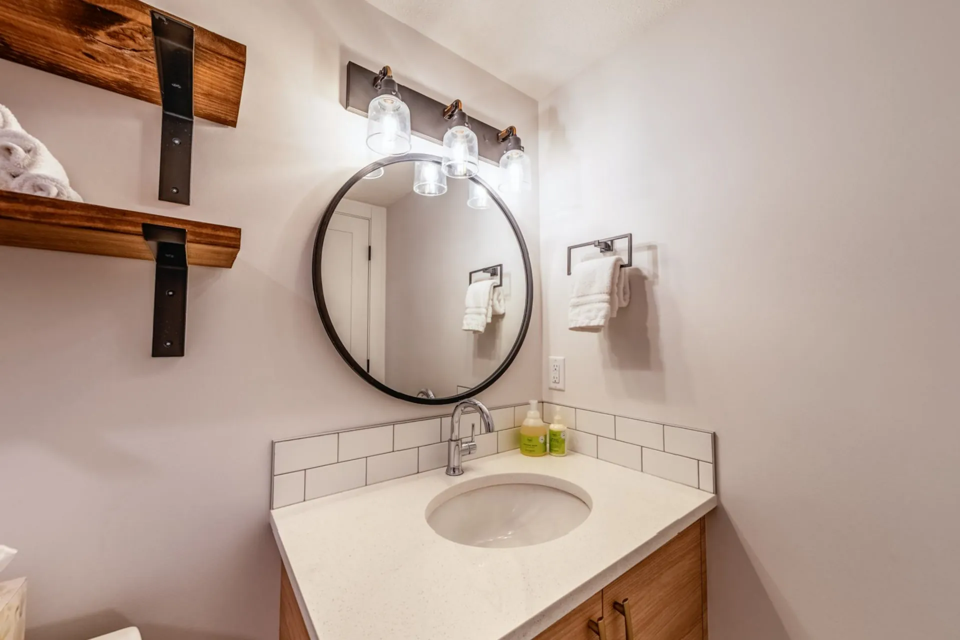 A bathroom with a round mirror, white subway tile and a timber vanity