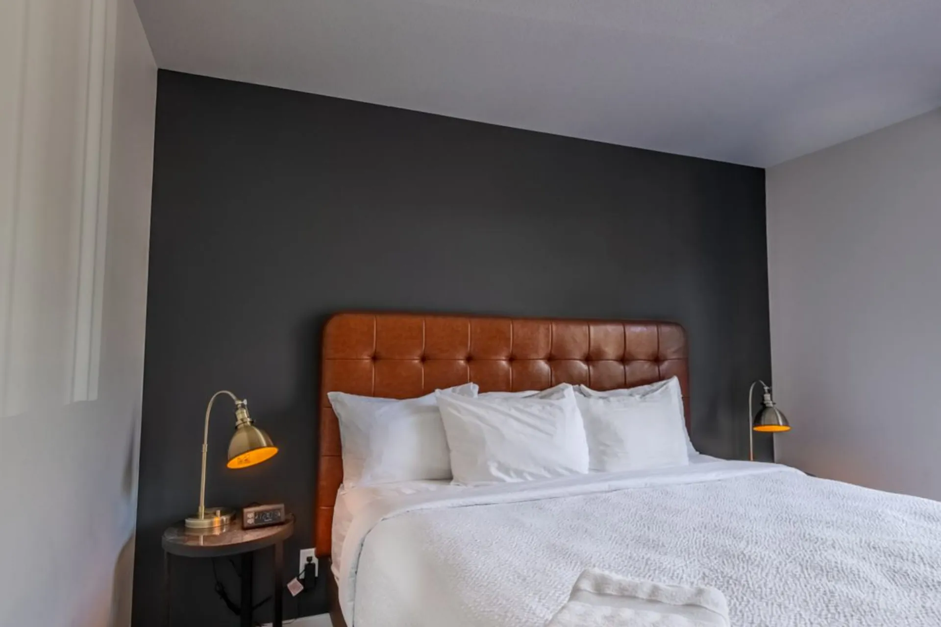 A bedroom with a tufted leather headboard, dark feature wall and brass reading lamps