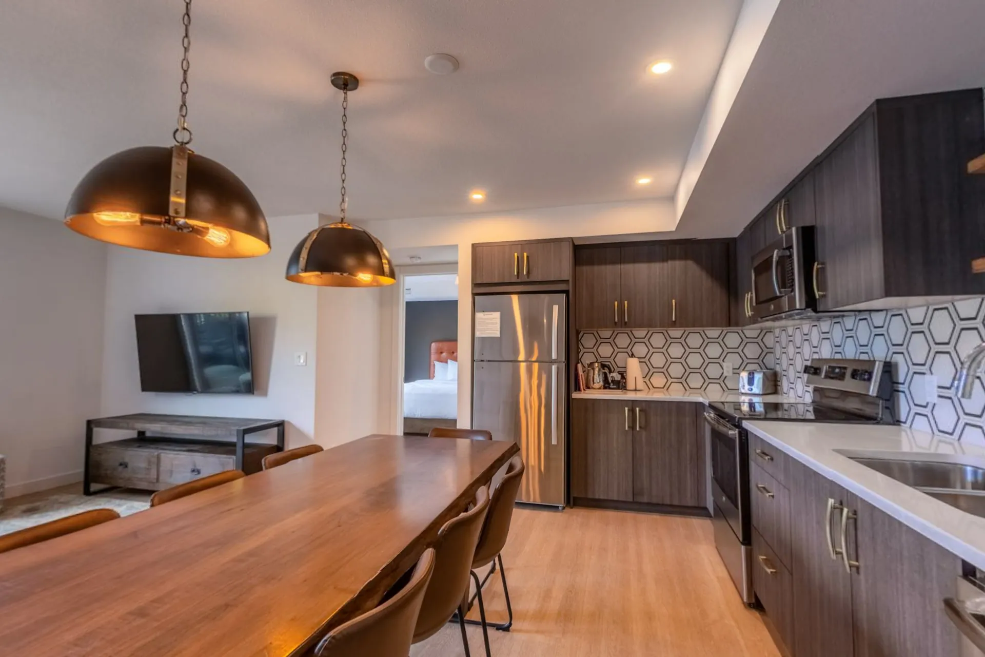 The three-bedroom apartment's dining table under copper pendants with the kitchen and living area beyond