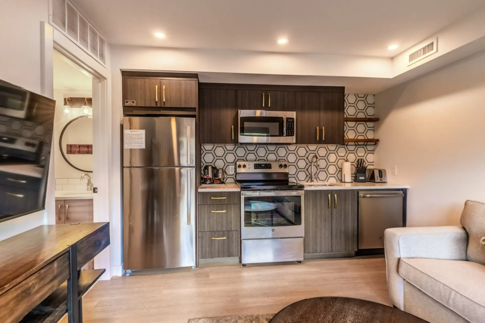 A micro suite's kitchen with stainless appliances, patterned tile and a sofa by the window