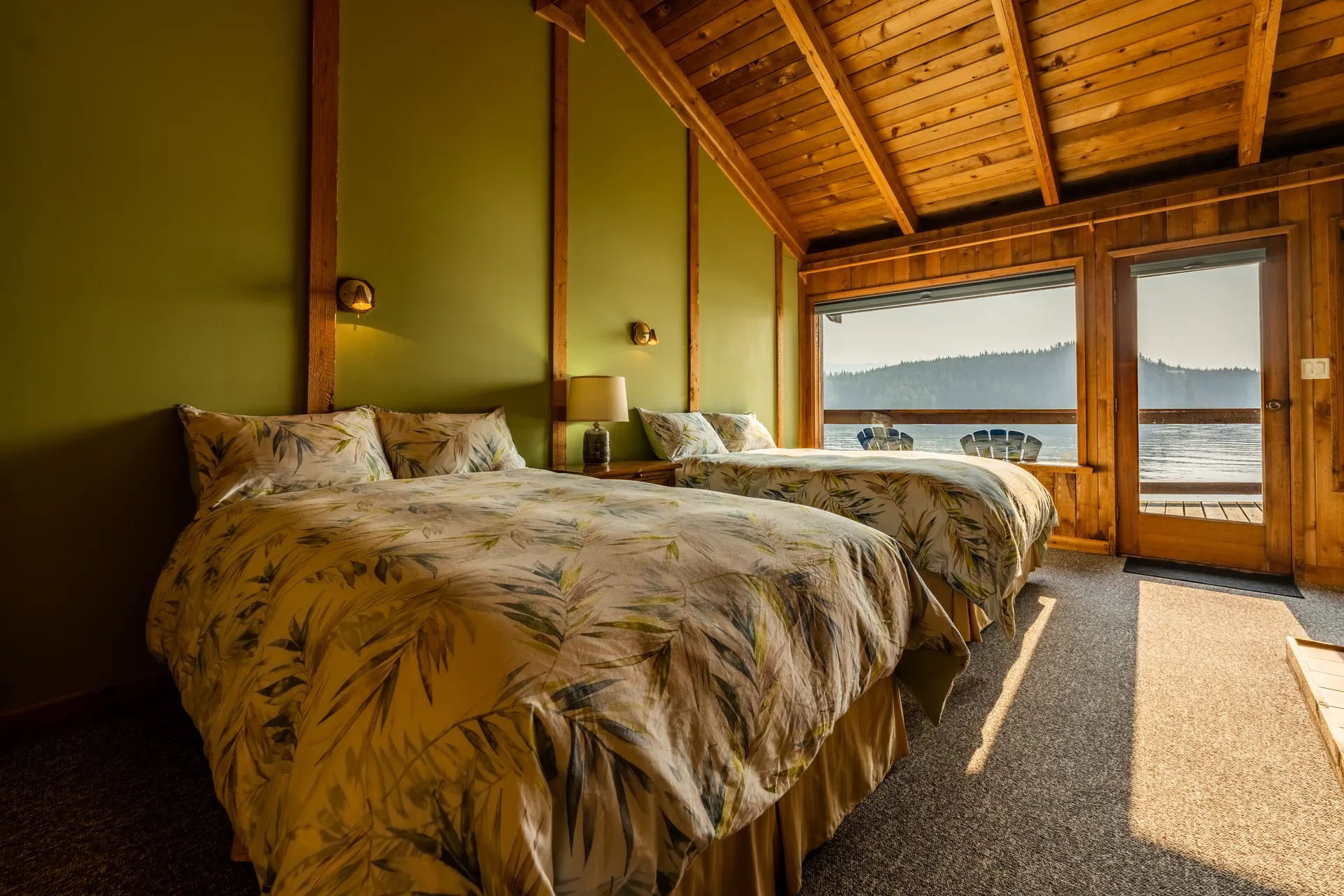 Green-walled guest room with two beds and a glass door onto the deck, the water and islands beyond