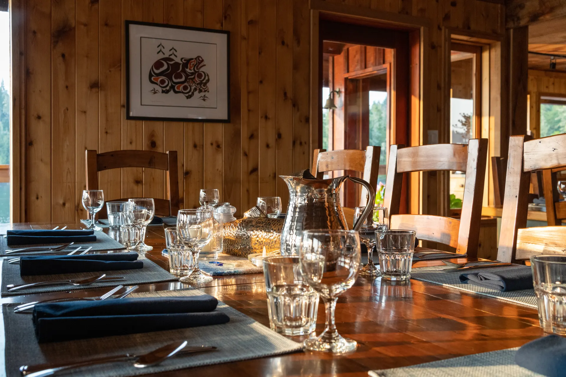 The dining table set with glassware and cloth napkins beneath a framed First Nations print