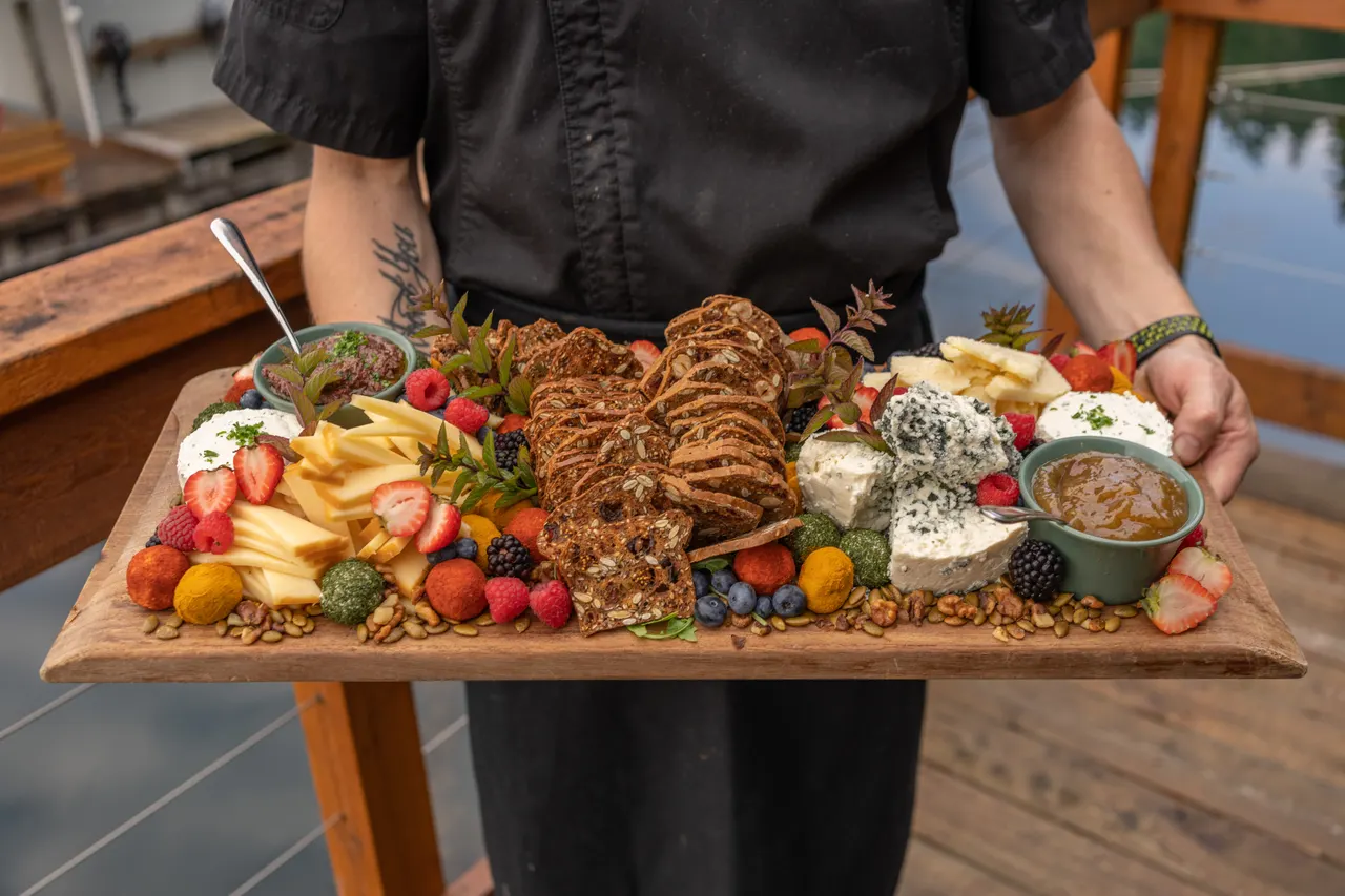 A chef carrying a wooden board loaded with cheeses, fruit, crackers and dips across the deck