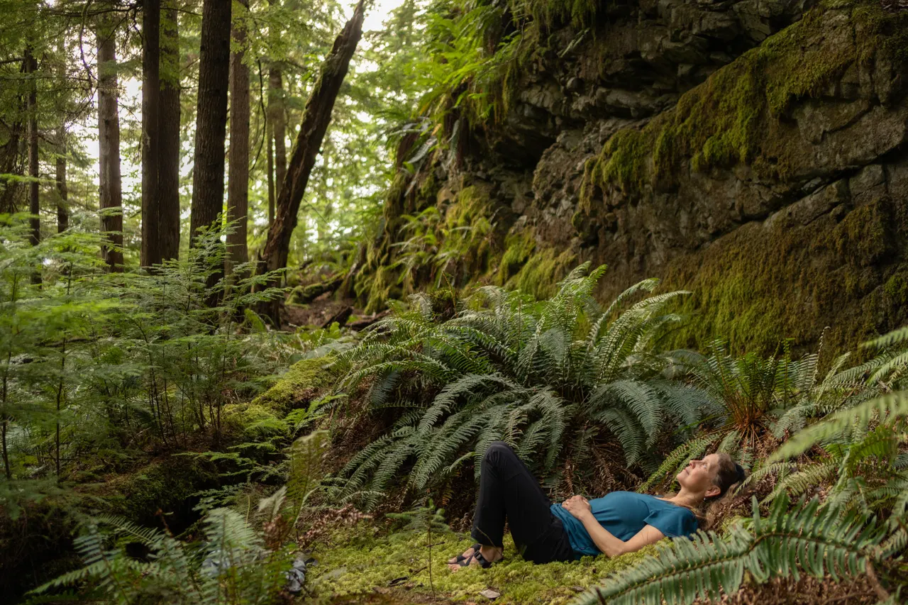 A guest lying back among ferns beneath a moss-covered rock face in the island's rainforest