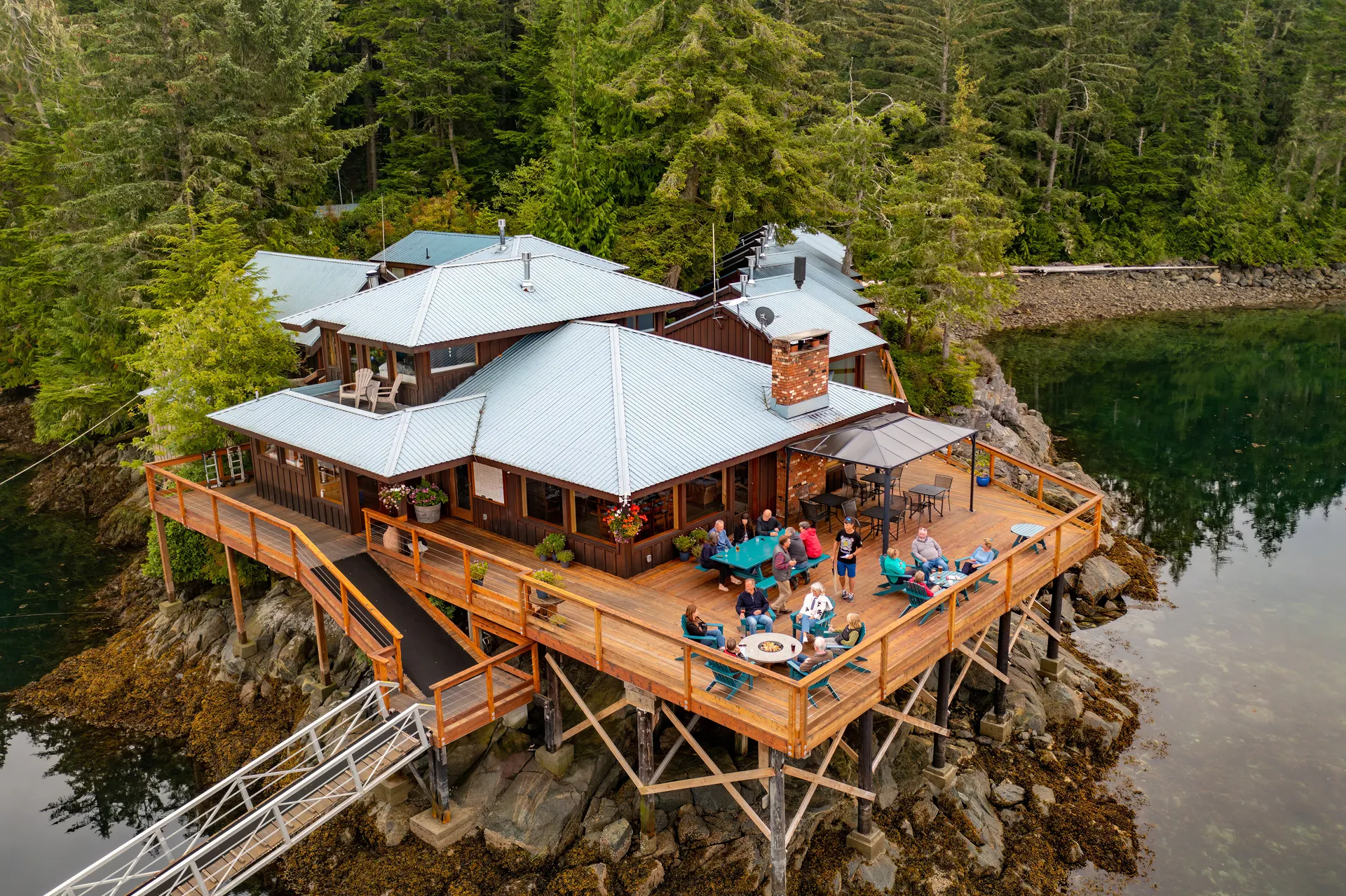 Aerial view of the main lodge on its rocky point, guests gathered on the deck and the ramp running down to the floating lodge