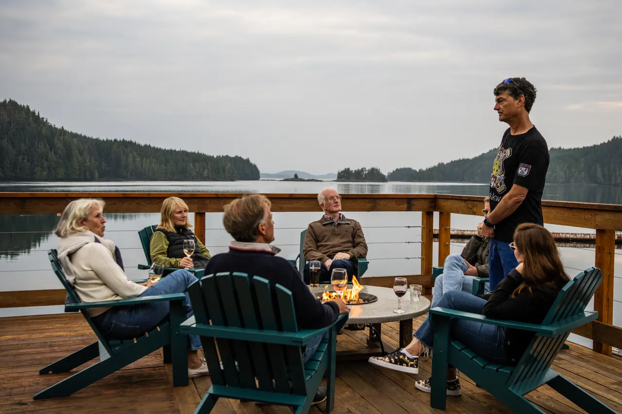 Five guests with glasses of wine around a fire table on the deck at sunset, the islands of the archipelago behind them