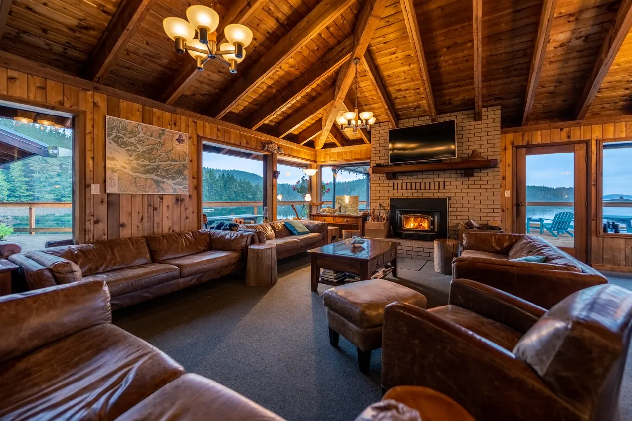 The lodge lounge with leather sofas and armchairs around a brick fireplace, under a timber cathedral ceiling
