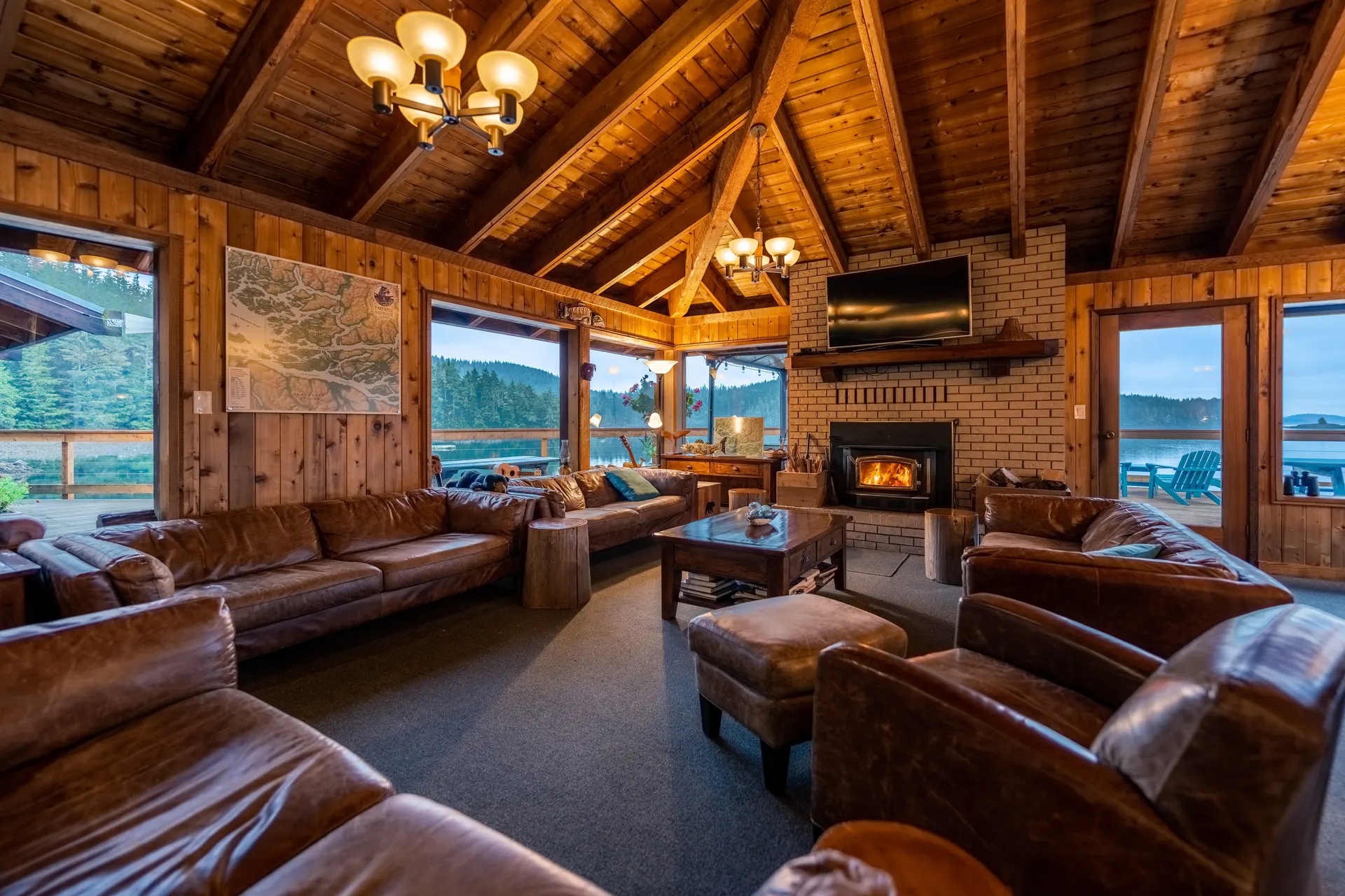 The lodge lounge with leather sofas and armchairs around a brick fireplace, under a timber cathedral ceiling