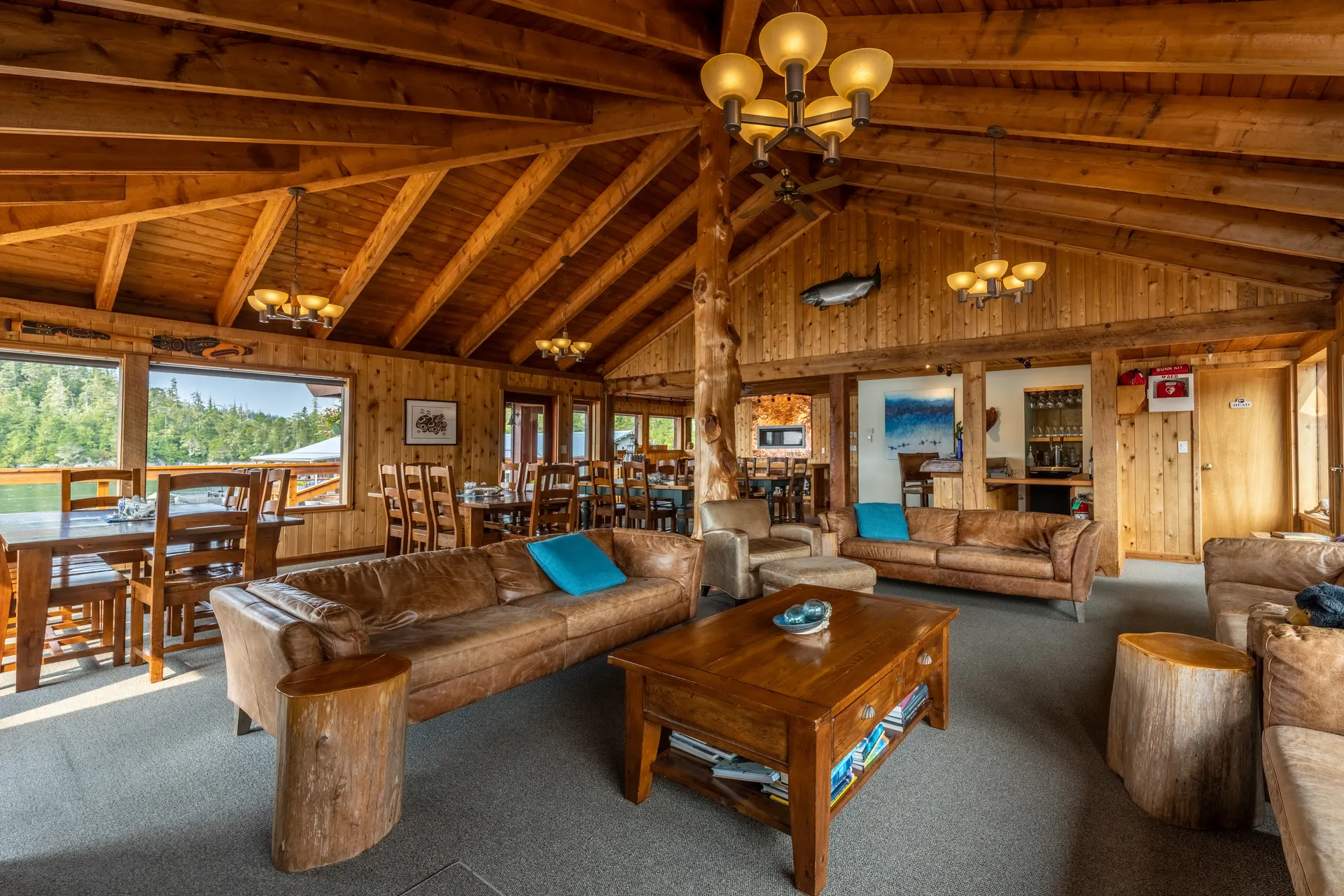 The main lodge's open-plan lounge and dining room, leather sofas and log-post beams with windows onto the water