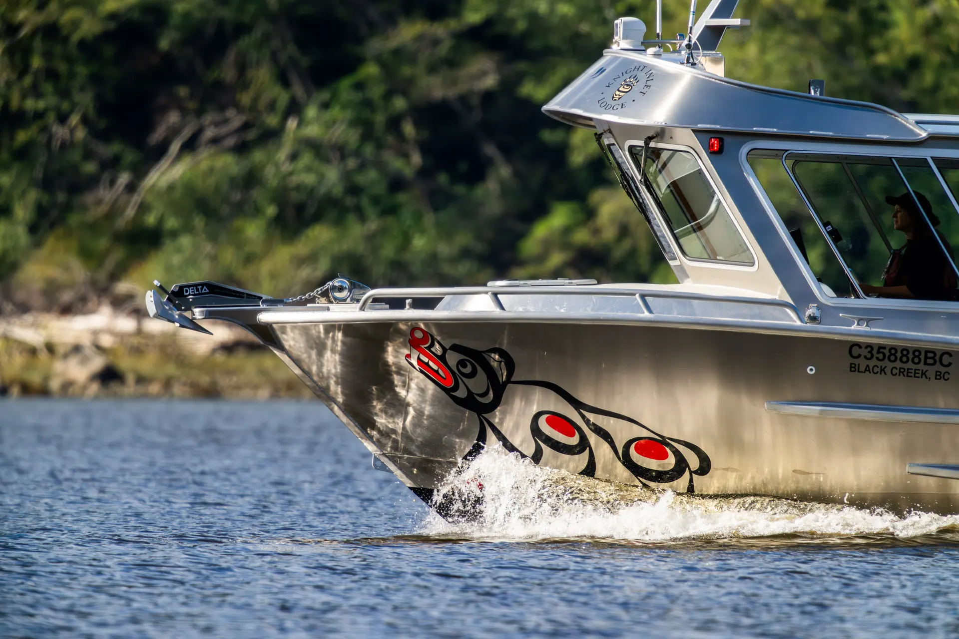 Knight Inlet Lodge's aluminium tour boat cutting through the water, a red and black First Nations formline bear painted on its bow