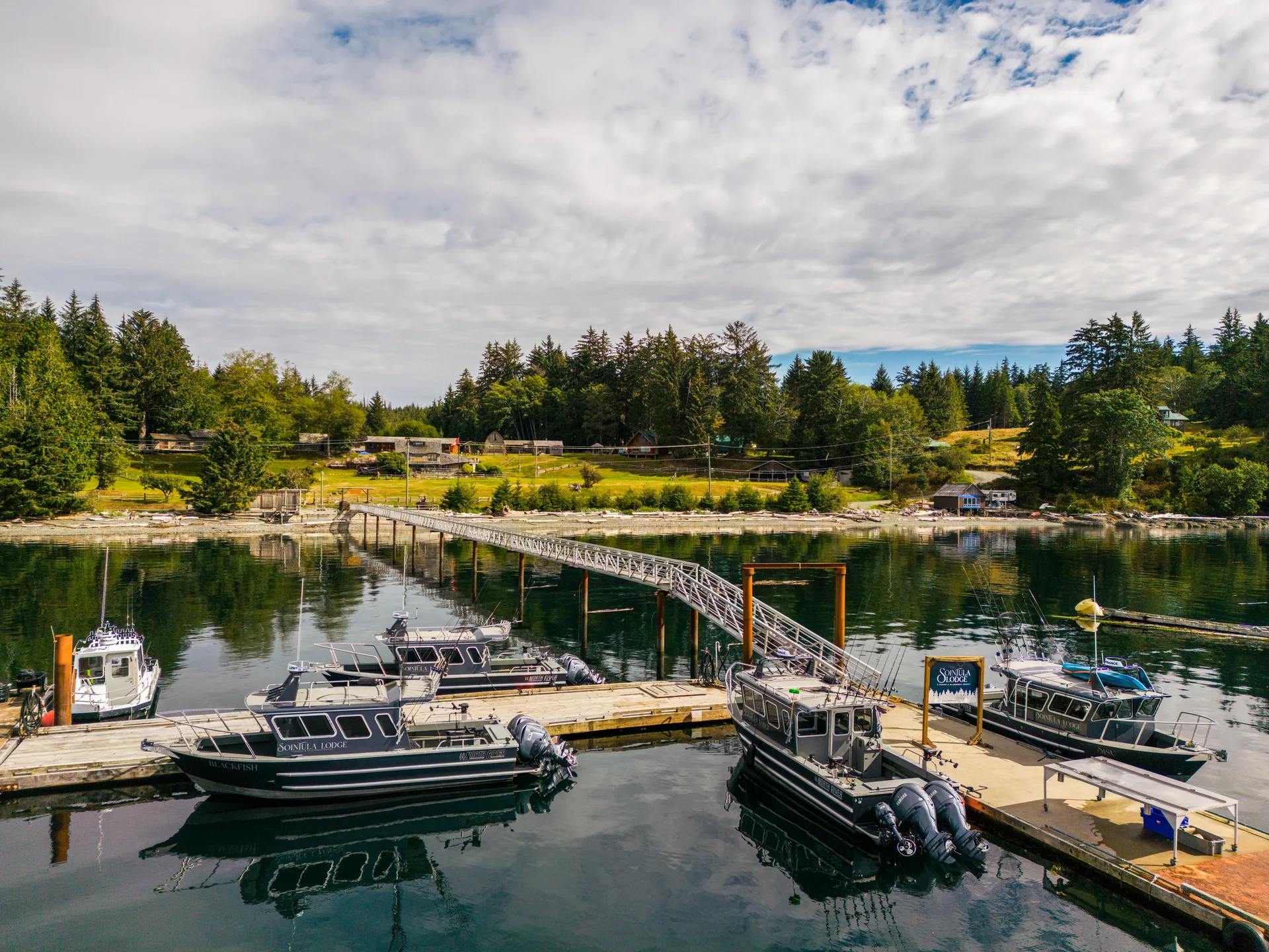 Aerial view of Sointula Lodge's dock and two guide boats in a sheltered cove, with the lodge and cabins in the trees behind