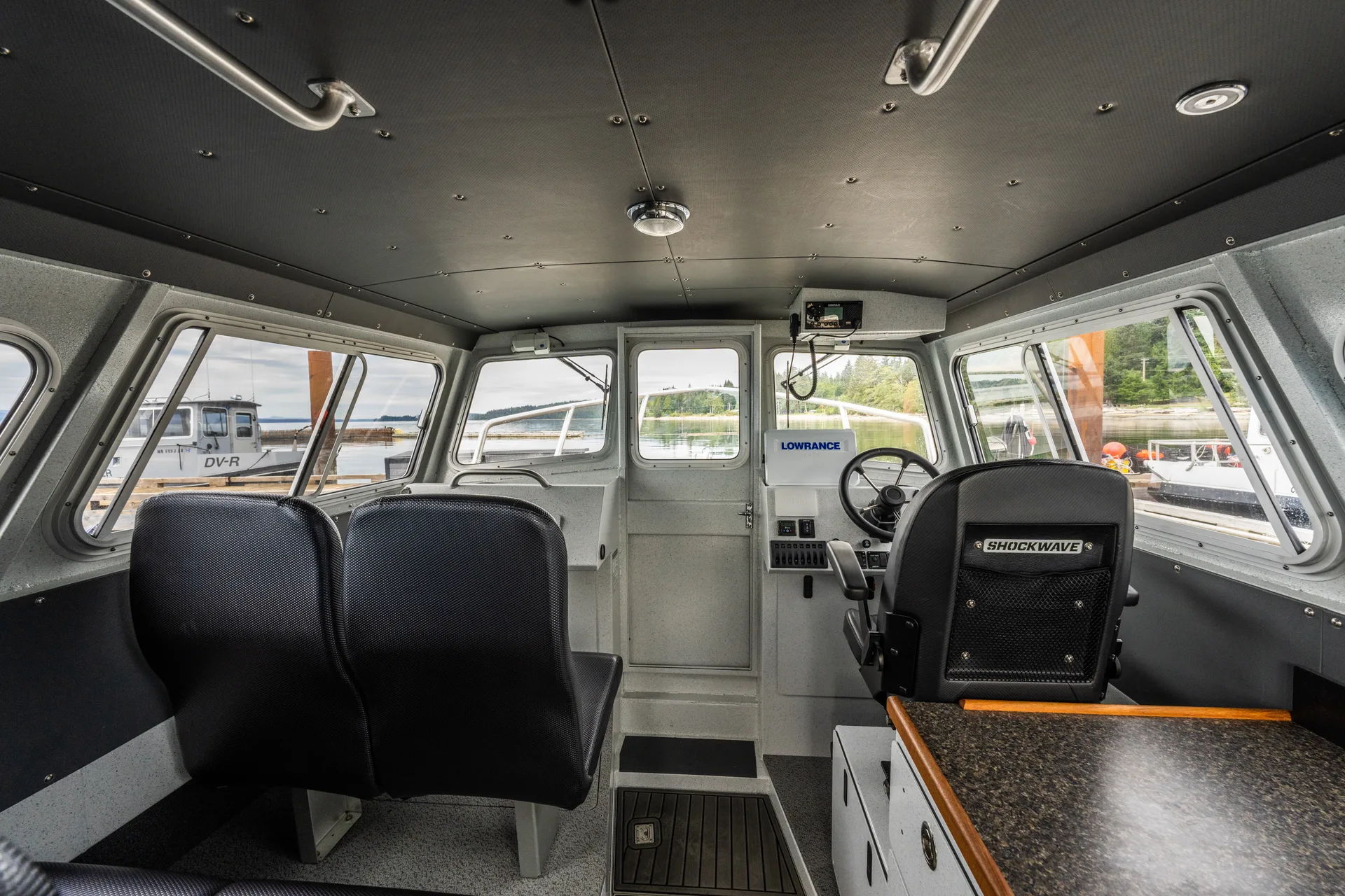 Inside the enclosed cabin of a guide boat: the helm, passenger seats and the dock through the windows