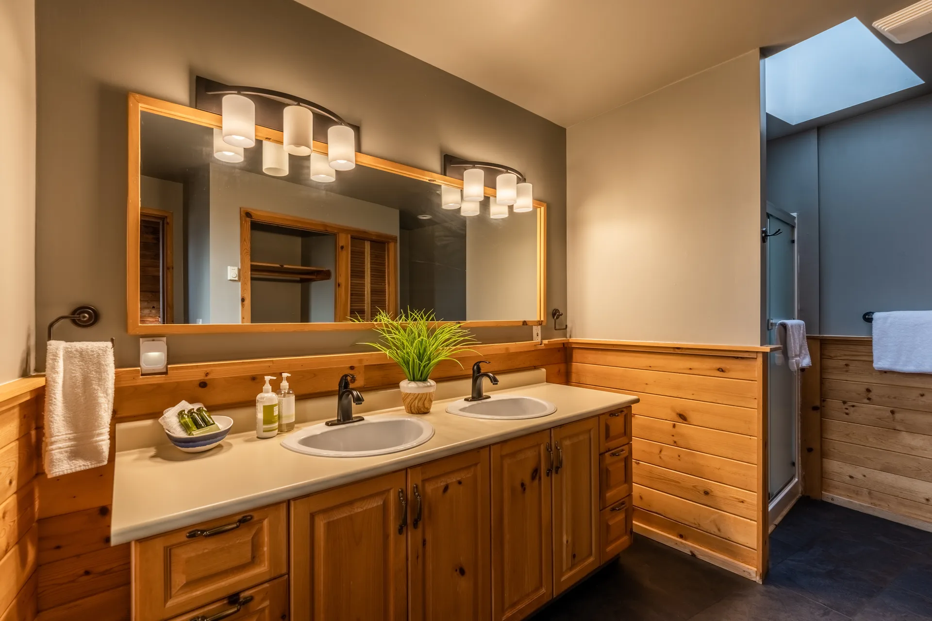 Cabin bathroom with a double vanity, wood cabinetry, a lit mirror and a walk-in shower