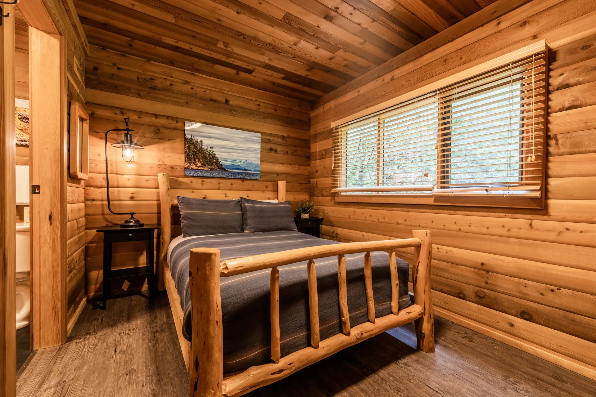 Log cabin bedroom with a log-frame bed under a window and a framed coastal photograph