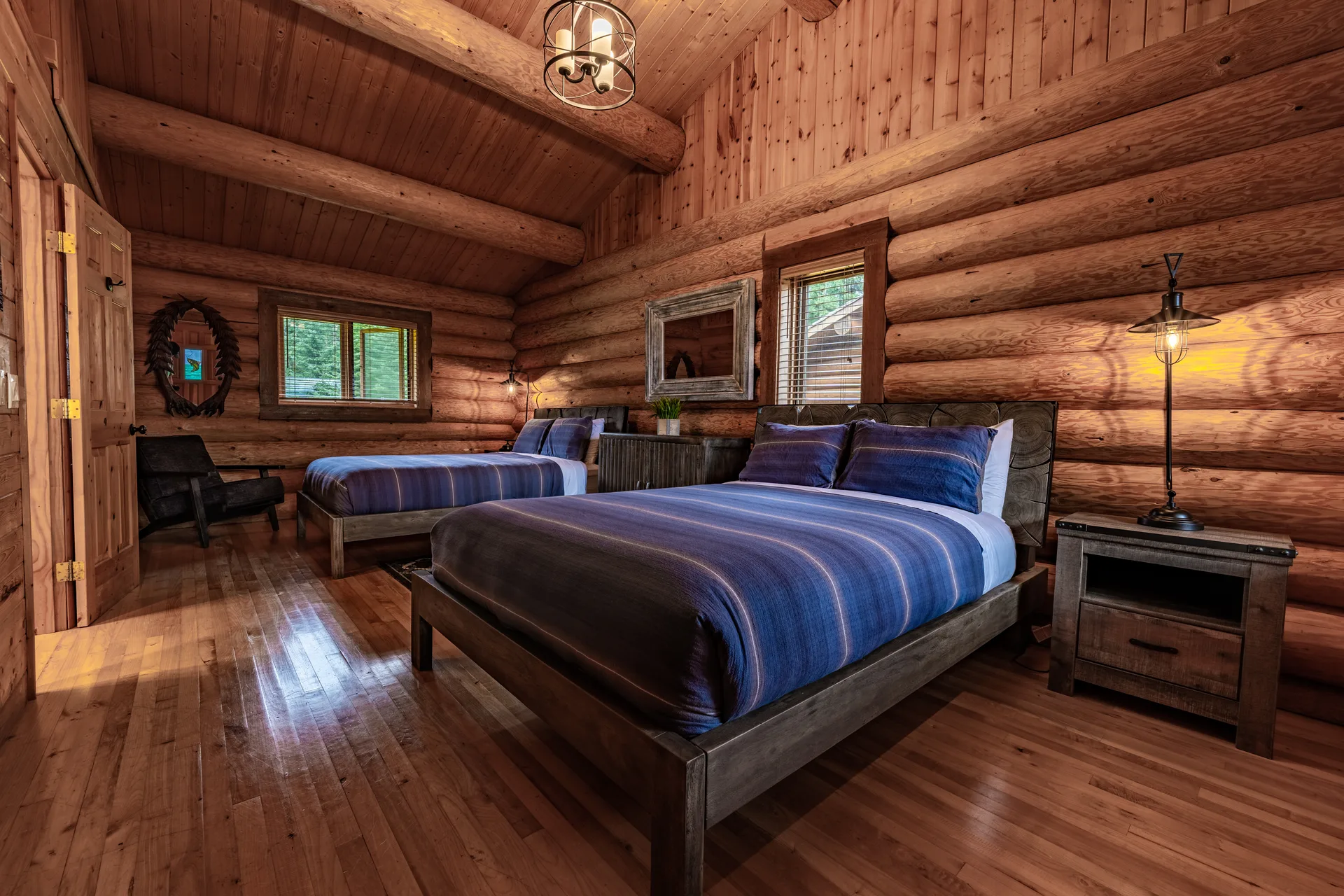 Log cabin bedroom with a bed in blue striped bedding, a round mirror and two windows