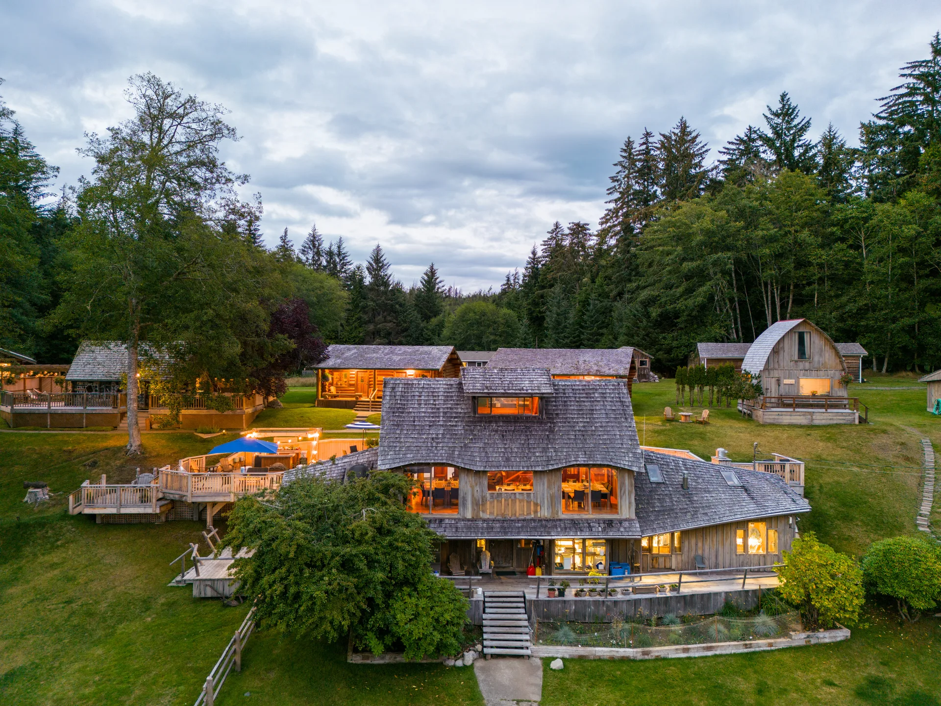 The main lodge lit from within at dusk, seen from the air with the dock and boardwalk in front of it