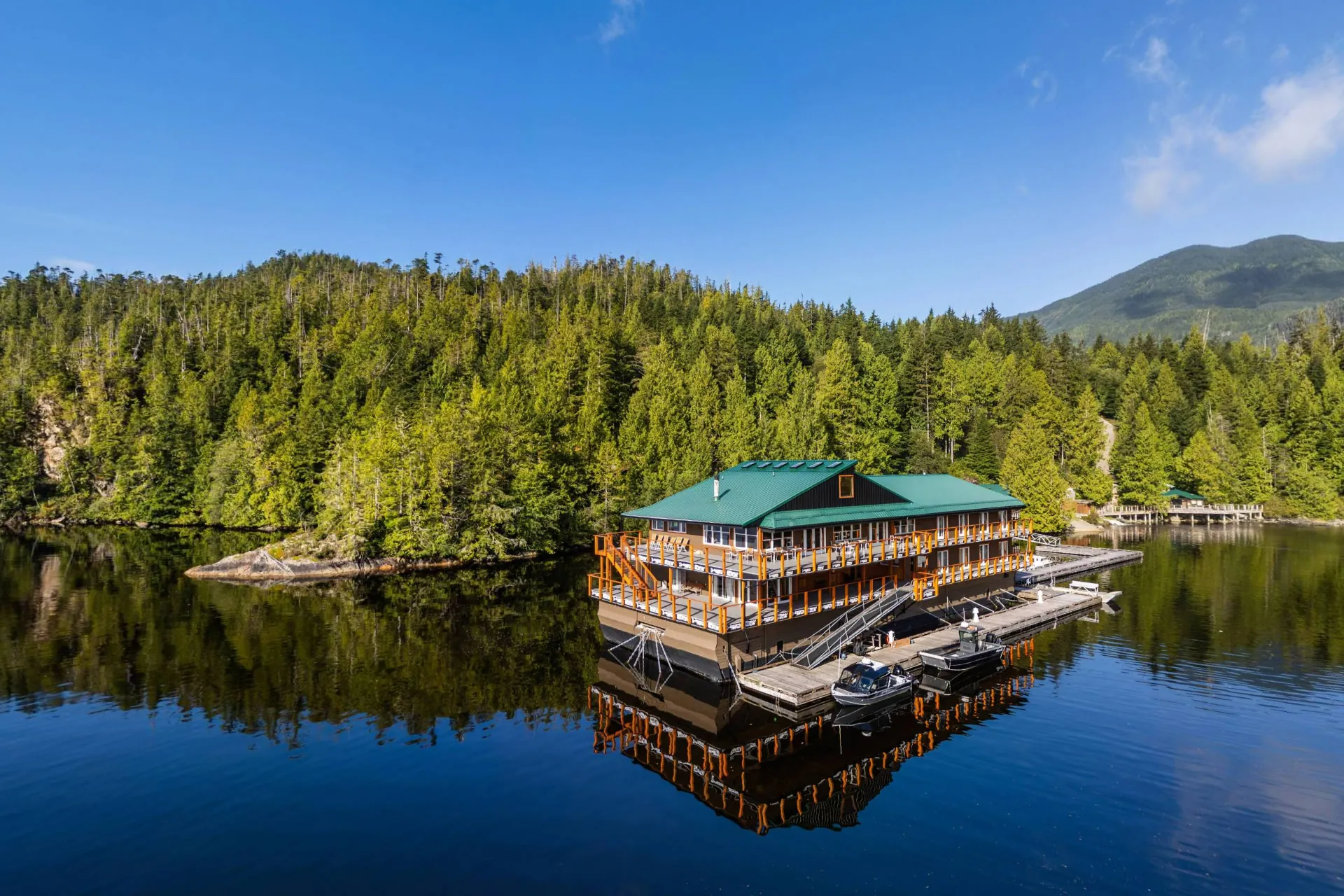 The floating lodge at Wahous from the water, its green roof and two decks of guest rooms moored below the rainforest in Quait Bay