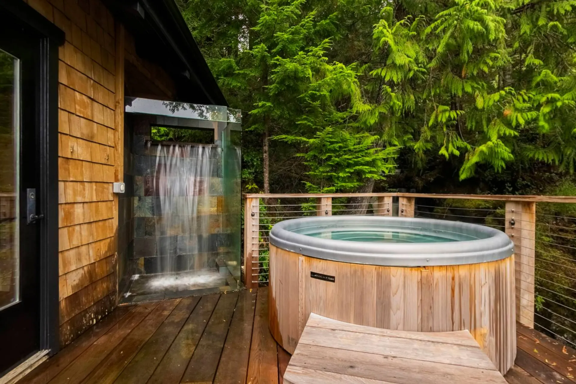 The cedar hot tub on the spa deck with a waterfall shower beside it and the rainforest pressing in