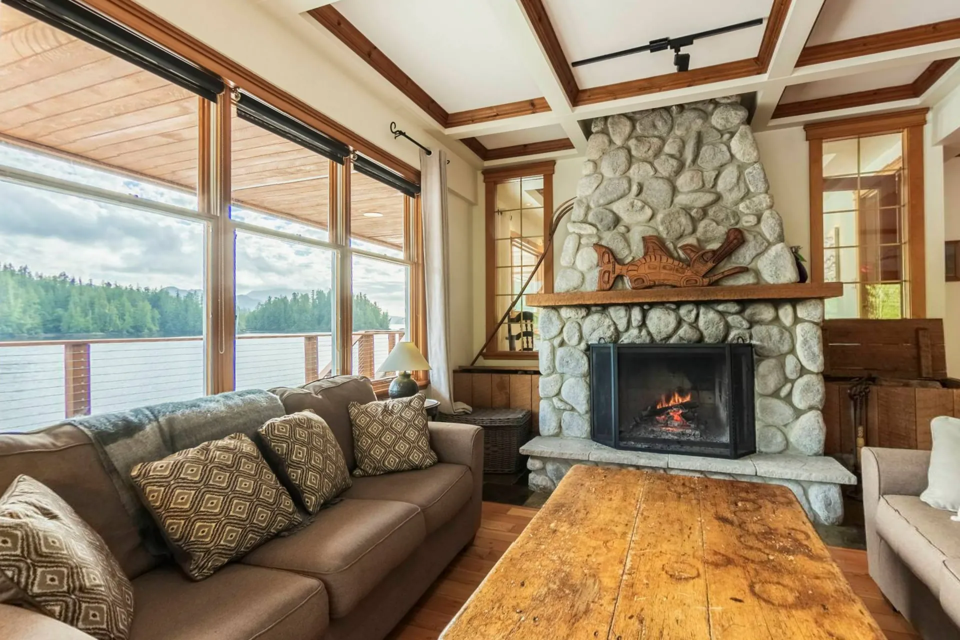 A guest room lounge with a stone fireplace, a sofa and the water through the windows