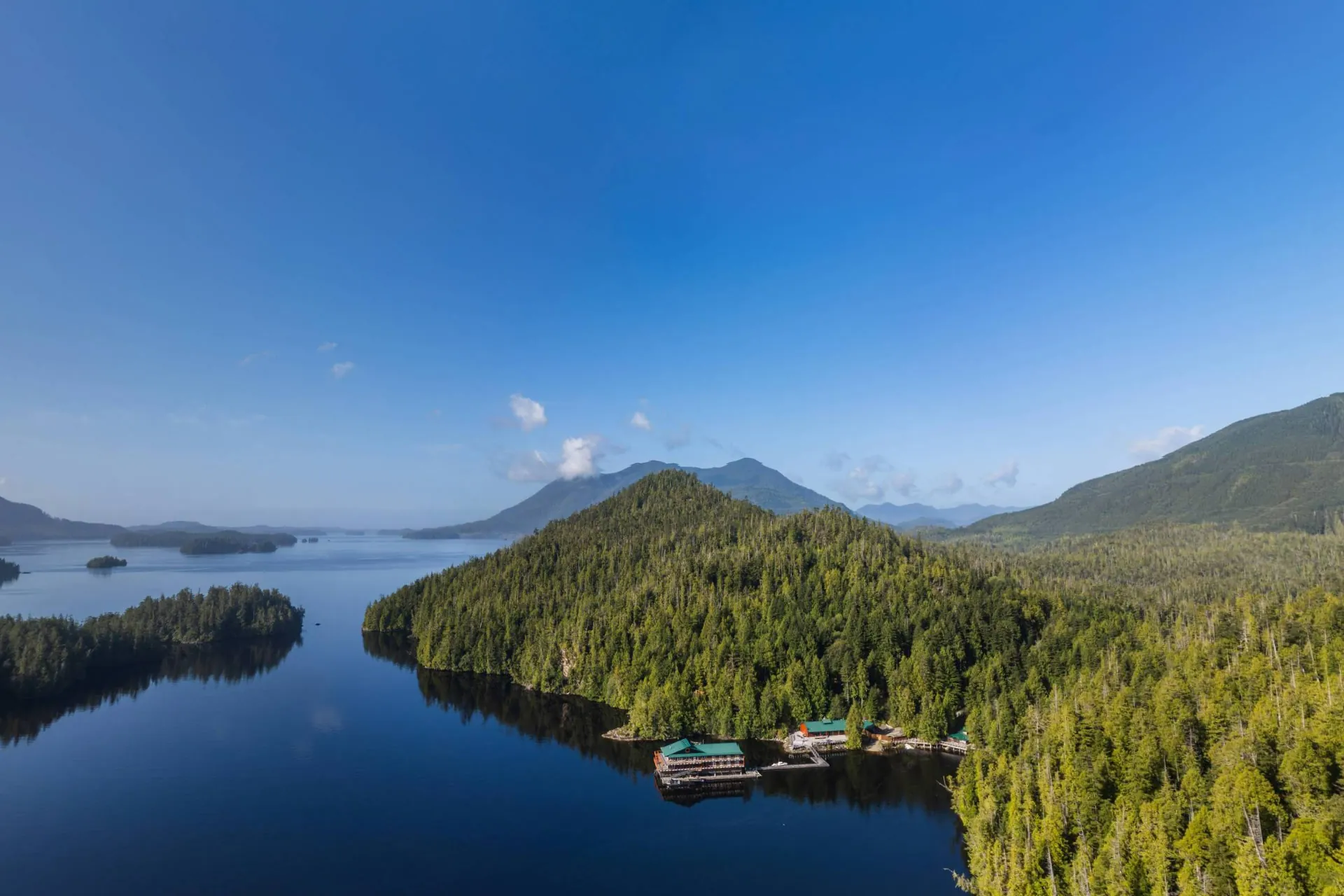 Quait Bay from the air, the floating lodge a small green roof at the foot of the forested hills with Clayoquot Sound beyond