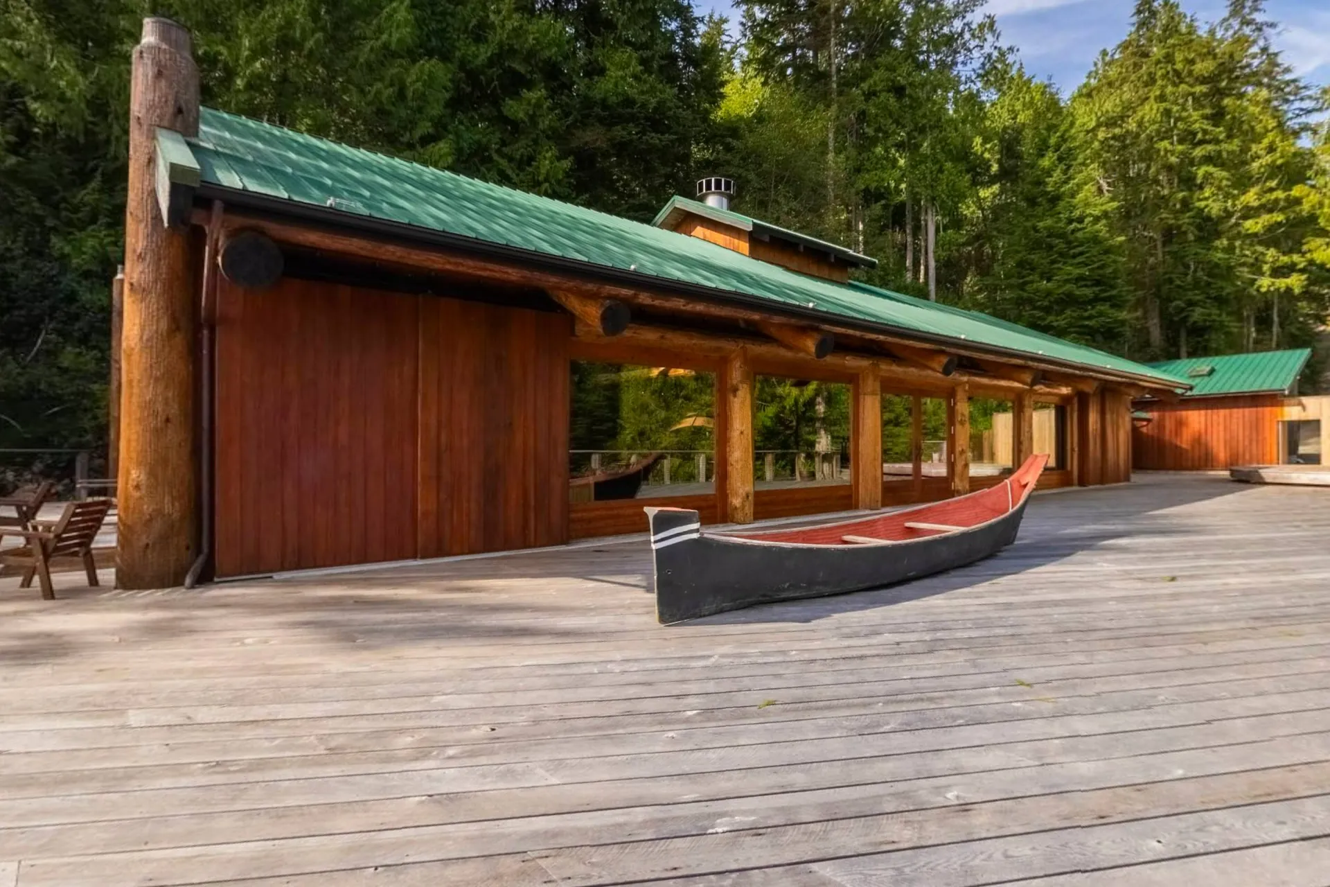 The longhouse from its deck, the cedar building under a green roof with a dugout canoe drawn up on the boards